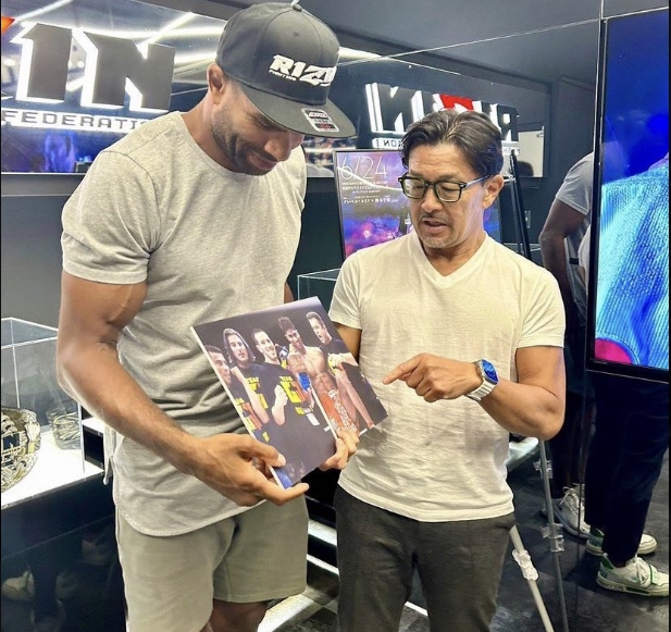 Alistair Overeem's noticeably leaner frame drew attention in photos from a post dated June 19, 2023, as he stood alongside another man and examined a signed combat sports photograph. Wearing a fitted gray T-shirt and shorts, the former heavyweight appeared considerably slimmer through his arms, shoulders, and legs than during his UFC years. The images offered fans an early look at the physical transformation that followed significant changes to his diet and lifestyle. | Source: X/COMBAT SPORTS TODAY