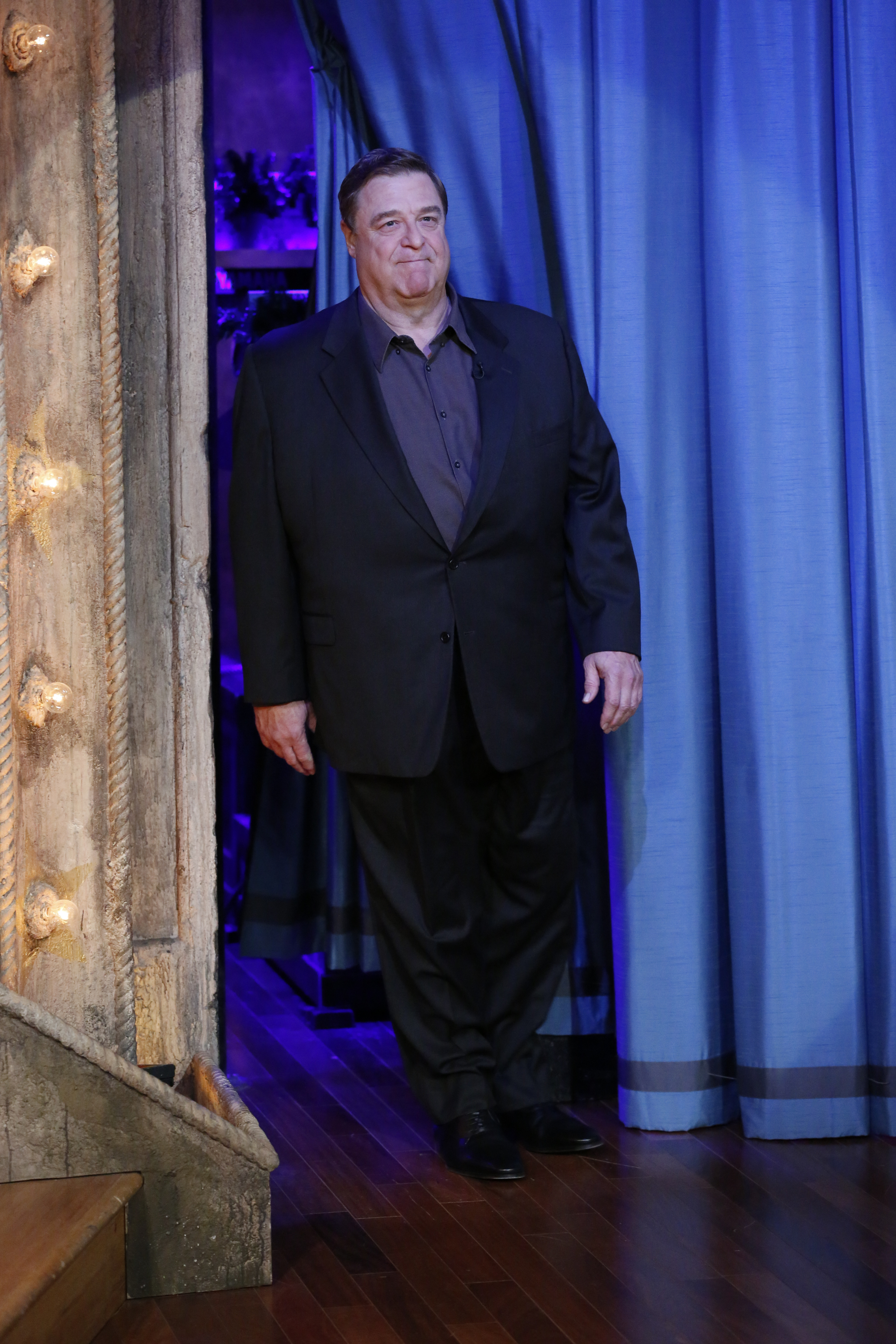 Goodman had a late night with Jimmy Fallon during the show's 941st episode in 2013. Dressed in a dark colored shirt and black suit, he appeared behind a blue curtain in a tight lipped grin.