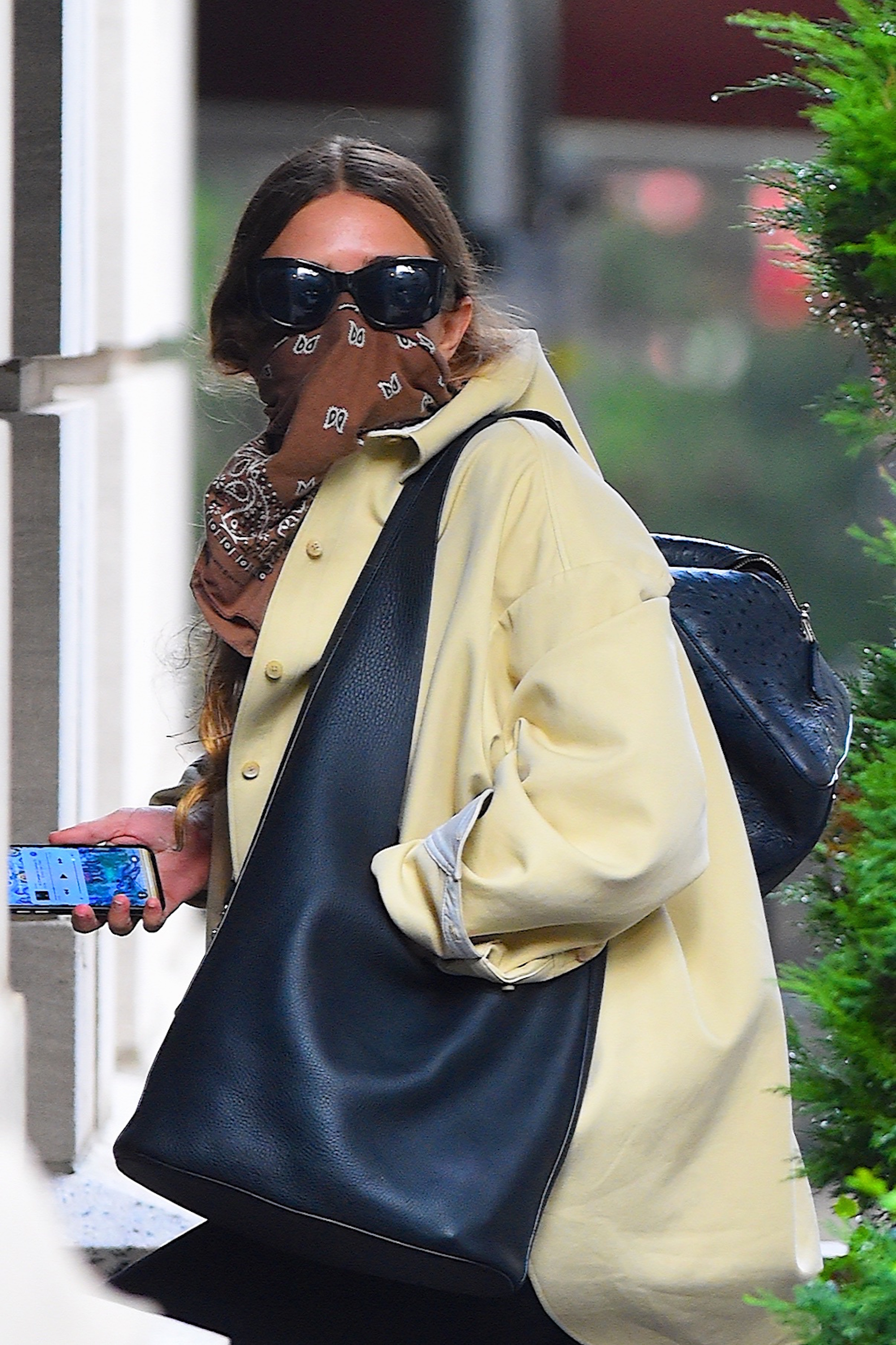Brown bandana fabric and oversized black sunglasses completely masked the facial contours of 34-year-old Ashley Olsen during an August 12, 2020 outing in Manhattan, leaving only her center-parted brunette hair visible. She embraced an effortlessly utilitarian silhouette with an oversized pale yellow shirt-jacket draped over one shoulder alongside a massive black leather hobo bag.