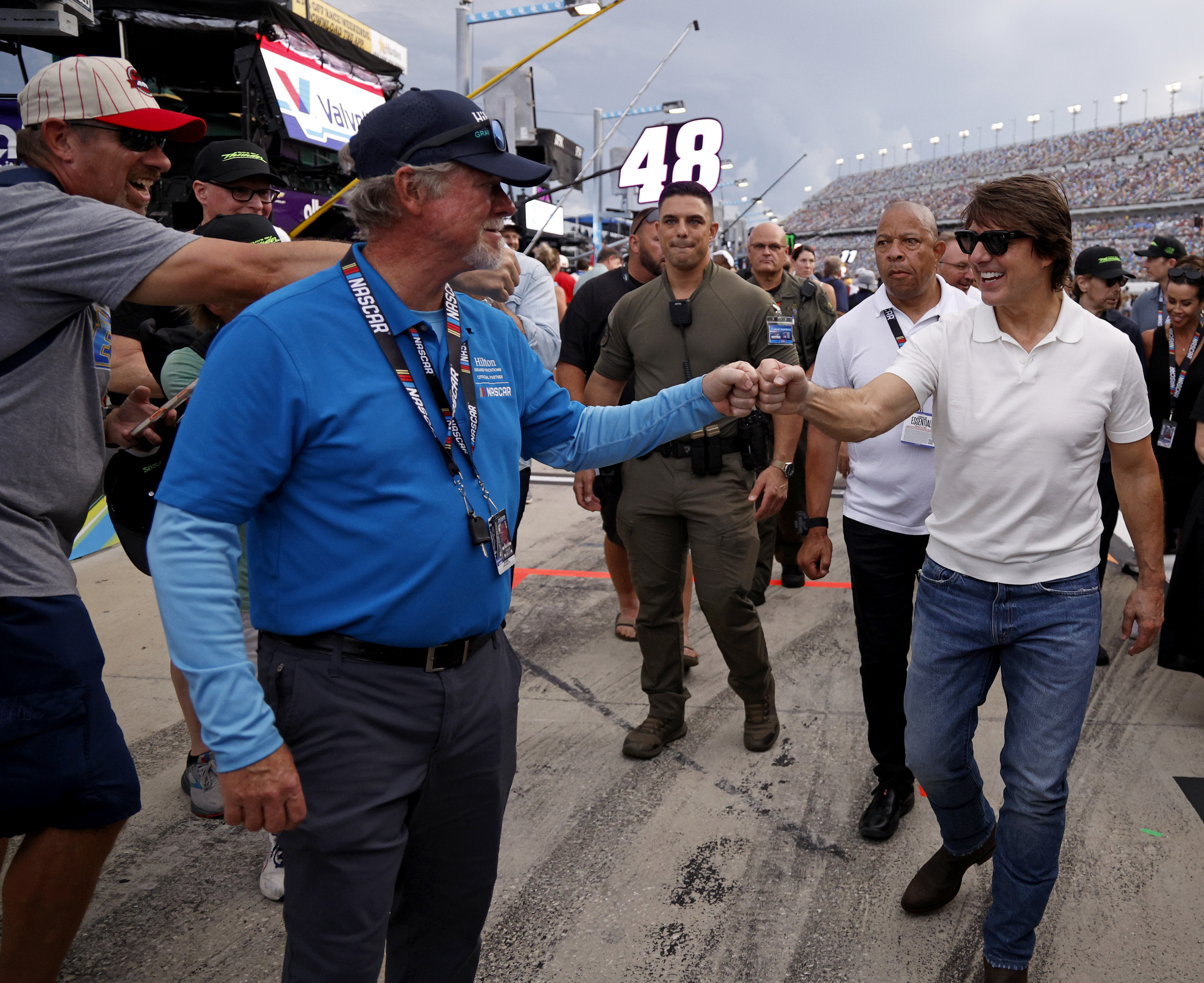 Cruise exchanges a fist bump while making his way through the busy track area at Daytona International Speedway. The actor smiles as NASCAR personnel and other attendees surround him ahead of the race. | Source: Getty Images