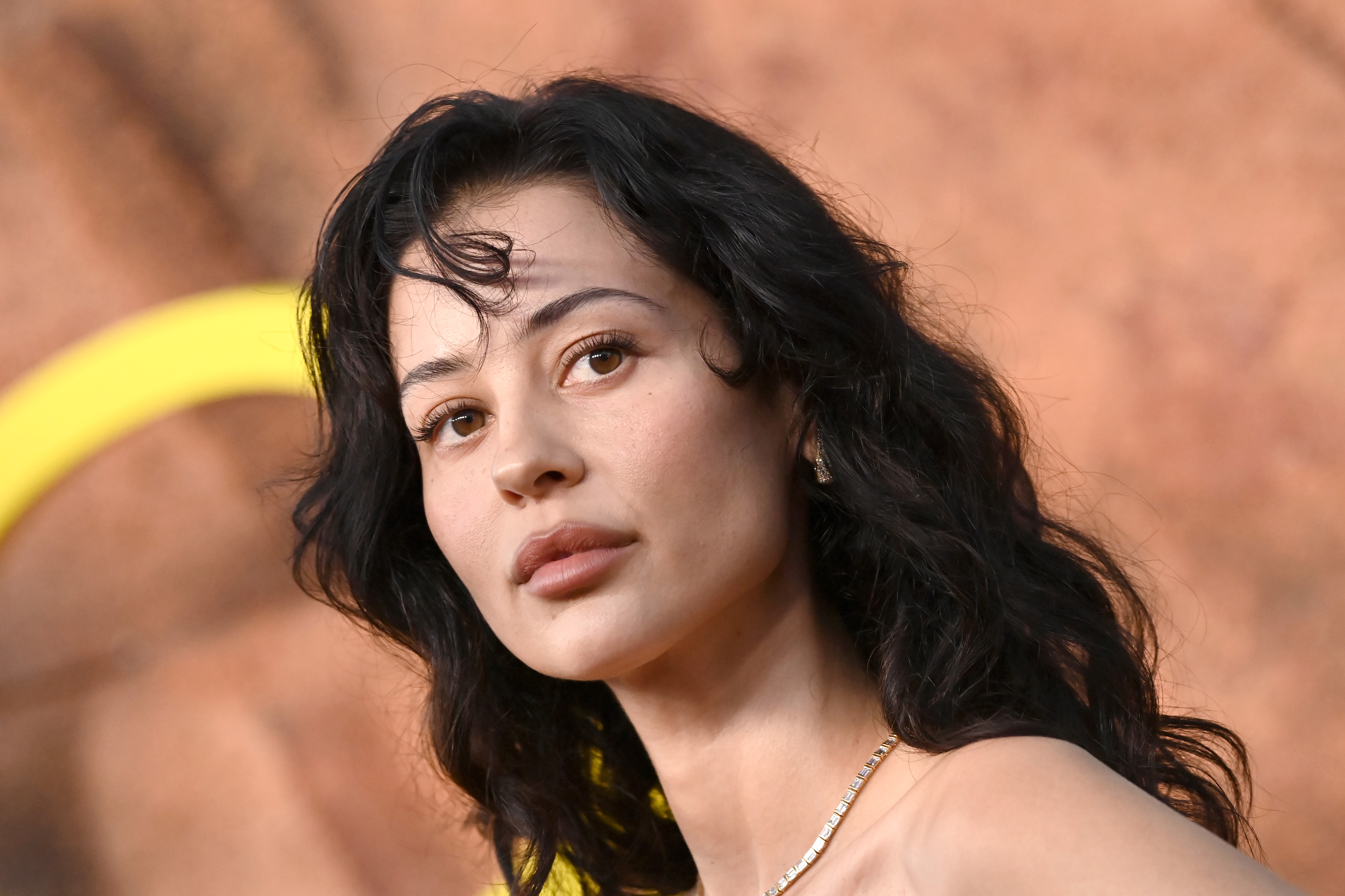 Alexa Demie exudes quiet intensity with softly tousled waves and a sculpted, luminous complexion. Her minimal makeup and warm-toned lips enhance her naturally striking features. A delicate necklace adds a subtle touch of elegance to the understated look.