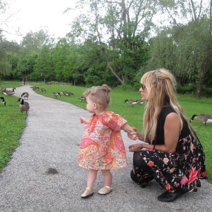 Nicole Richie crouches beside toddler Harlow Winter Kate Madden on a park path as geese gather nearby. Dressed in a bright patterned dress, Kate looks behind her while spending time outdoors with her mother. | Source: Instagram/nicolerichie and joelmadden
