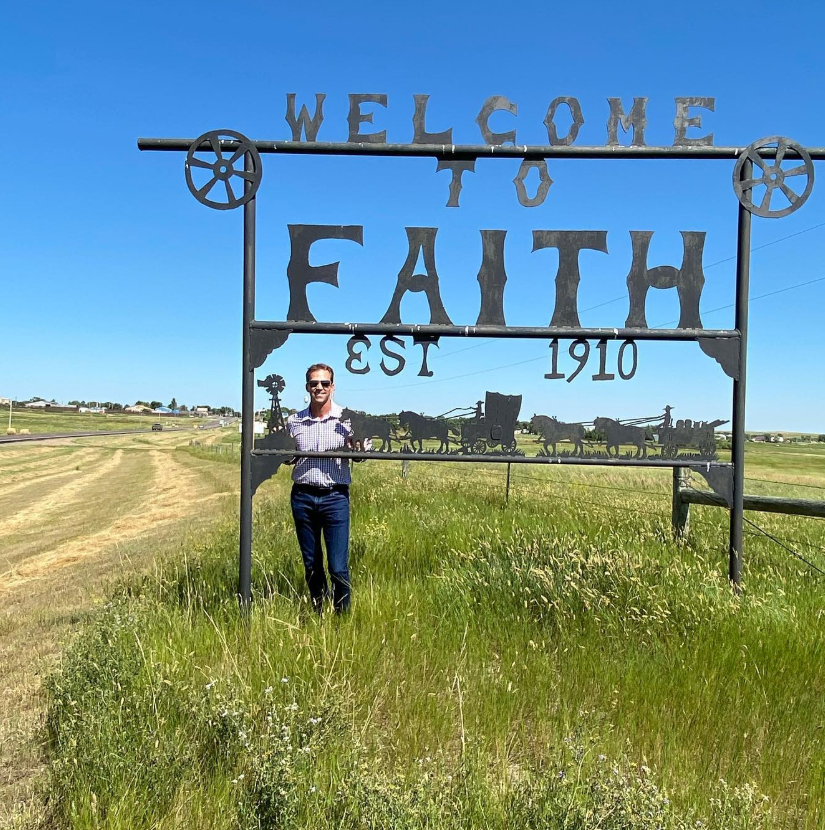 Framed by open prairie and big sky, Bryon Noem stands beneath a “Welcome to Faith” sign—small town roots, wide horizon. | Source: Instagram/sdbryonnoem