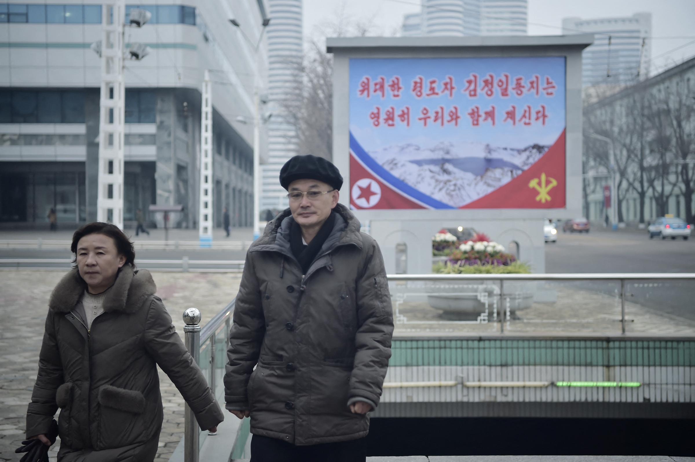 People walk by a poster in Pyongyang on February 16, 2025, marking Kim Jong Il's 83rd birthday | Source: Getty Images
