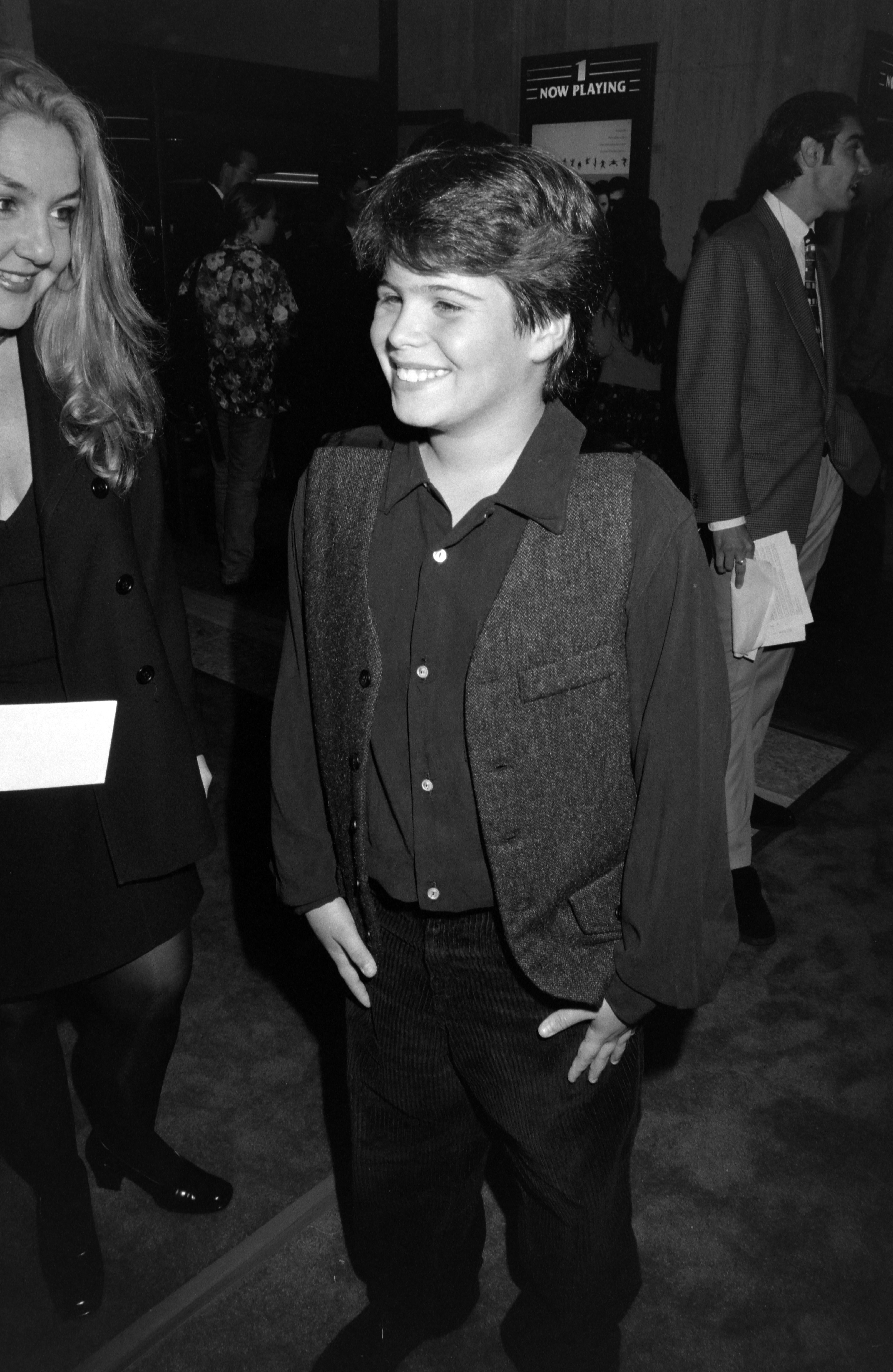 The young actor smiles at the premiere of That Thing You Do!, wearing a dark shirt and vest — a glimpse of how much he had grown since his breakthrough childhood role.