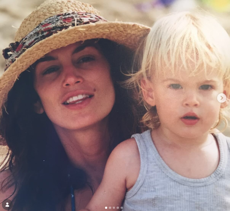 A sun-drenched beach memory posted on February 20, 2024, captured a smiling Cindy Crawford wearing a woven sunhat while holding toddler Presley close in a casual ribbed tank top. | Source: Instagram/presleygerber