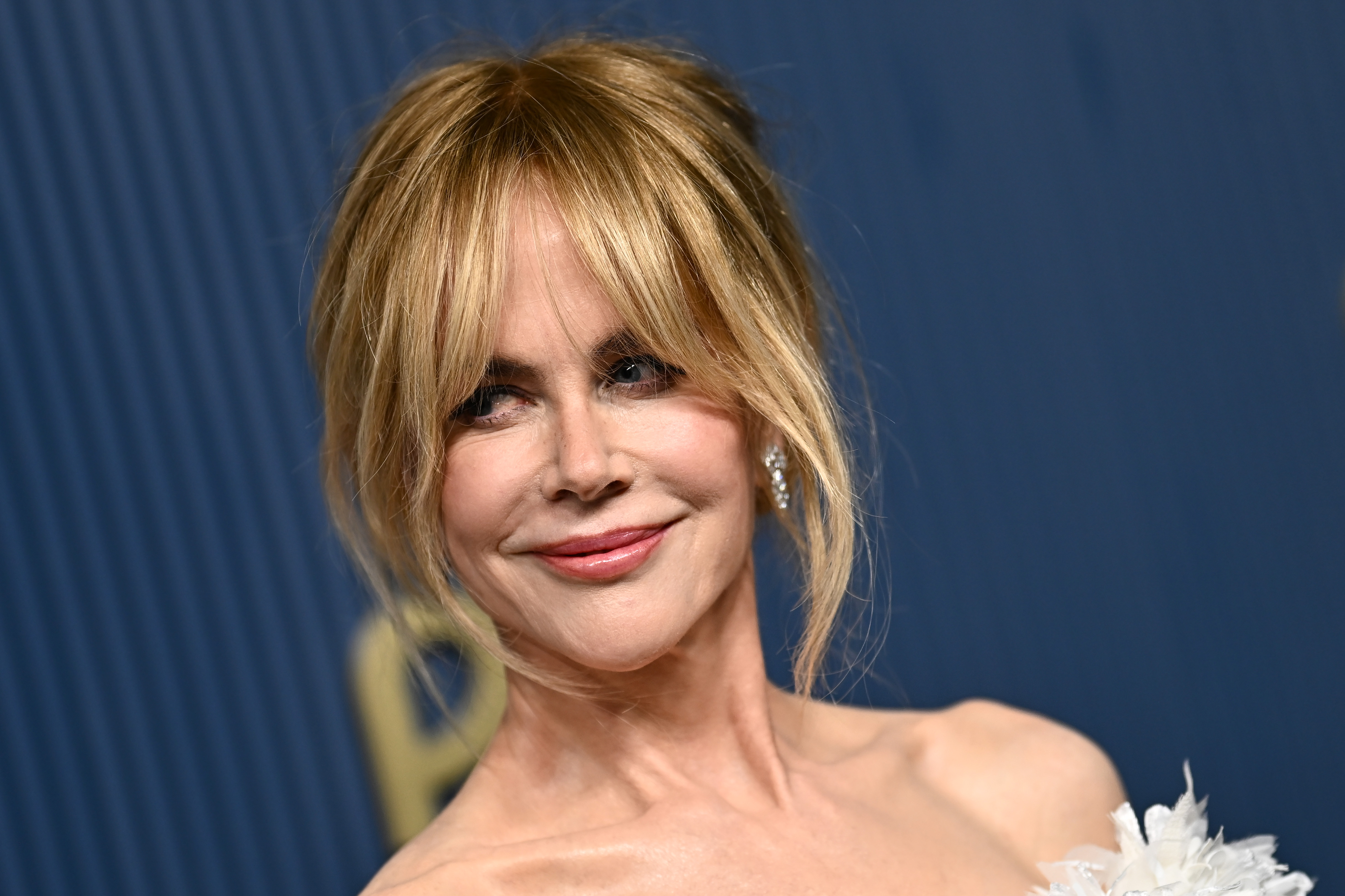 The portrait highlights Kidman's loose updo, face-framing bangs and soft pink lip color while showing only part of the gown. Its feathered neckline provides an early hint of the design before the full silhouette is revealed. | Source: Getty Images