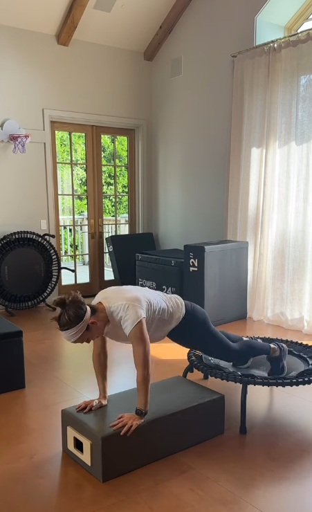 Jennifer Garner wears a white T-shirt, navy leggings, sneakers, and a white headband inside a bright home gym with wooden floors, large windows, and exercise equipment in the background.. | Source: Instagram/jennifer.garner