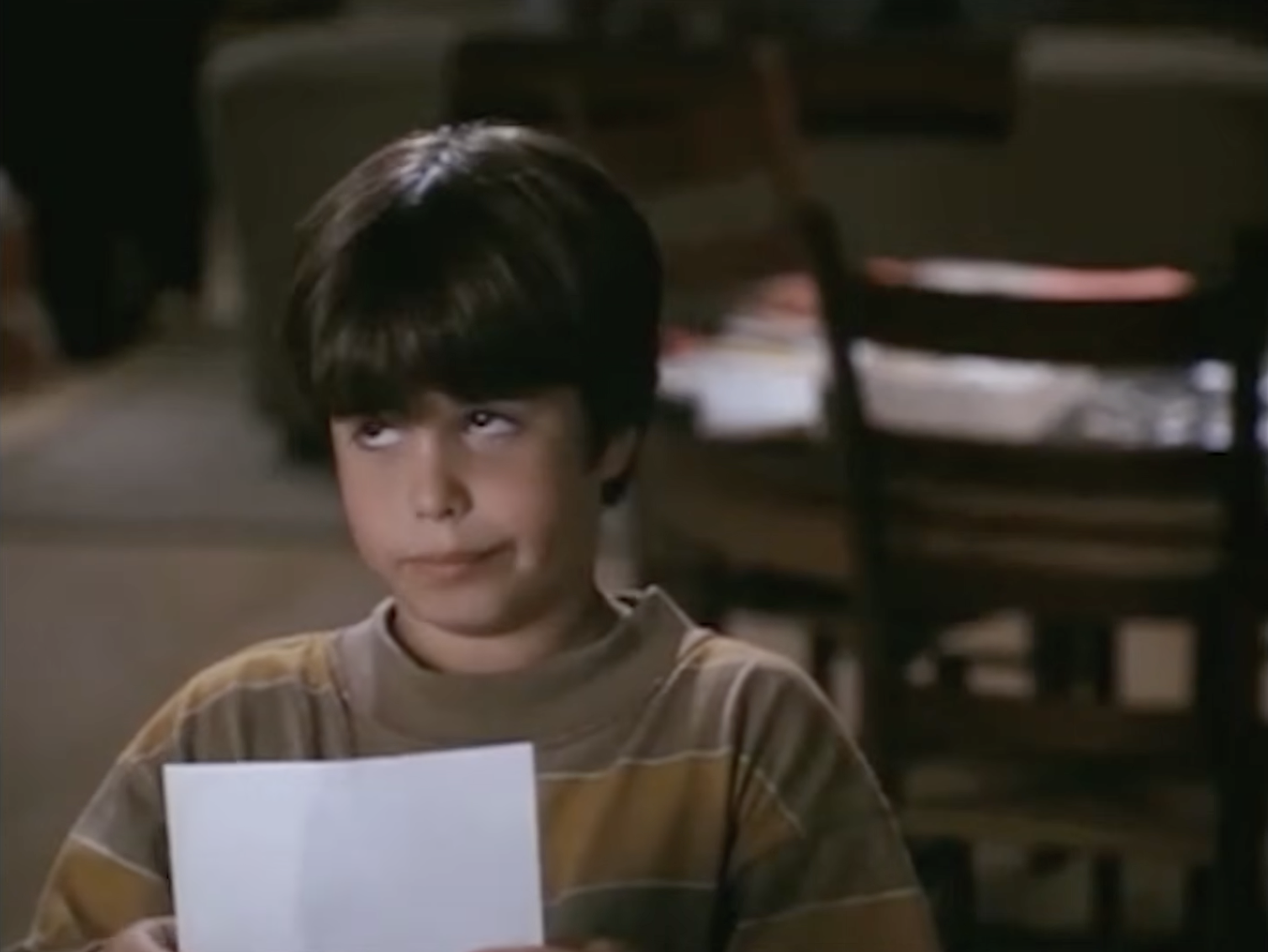 A young boy holds a piece of paper and gives a playful sideways glance in a scene from Sleepless in Seattle, capturing the expressive charm that made his character so memorable. | Source: Rotten Tomatoes Classic Trailers / YouTube.