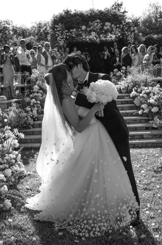 The bride and groom sealed their ceremony with a kiss as cheering guests looked on, with the bride’s flower-dotted gown and sweeping veil filling the romantic black-and-white frame. | Source: Instagram/dylanjaggerlee