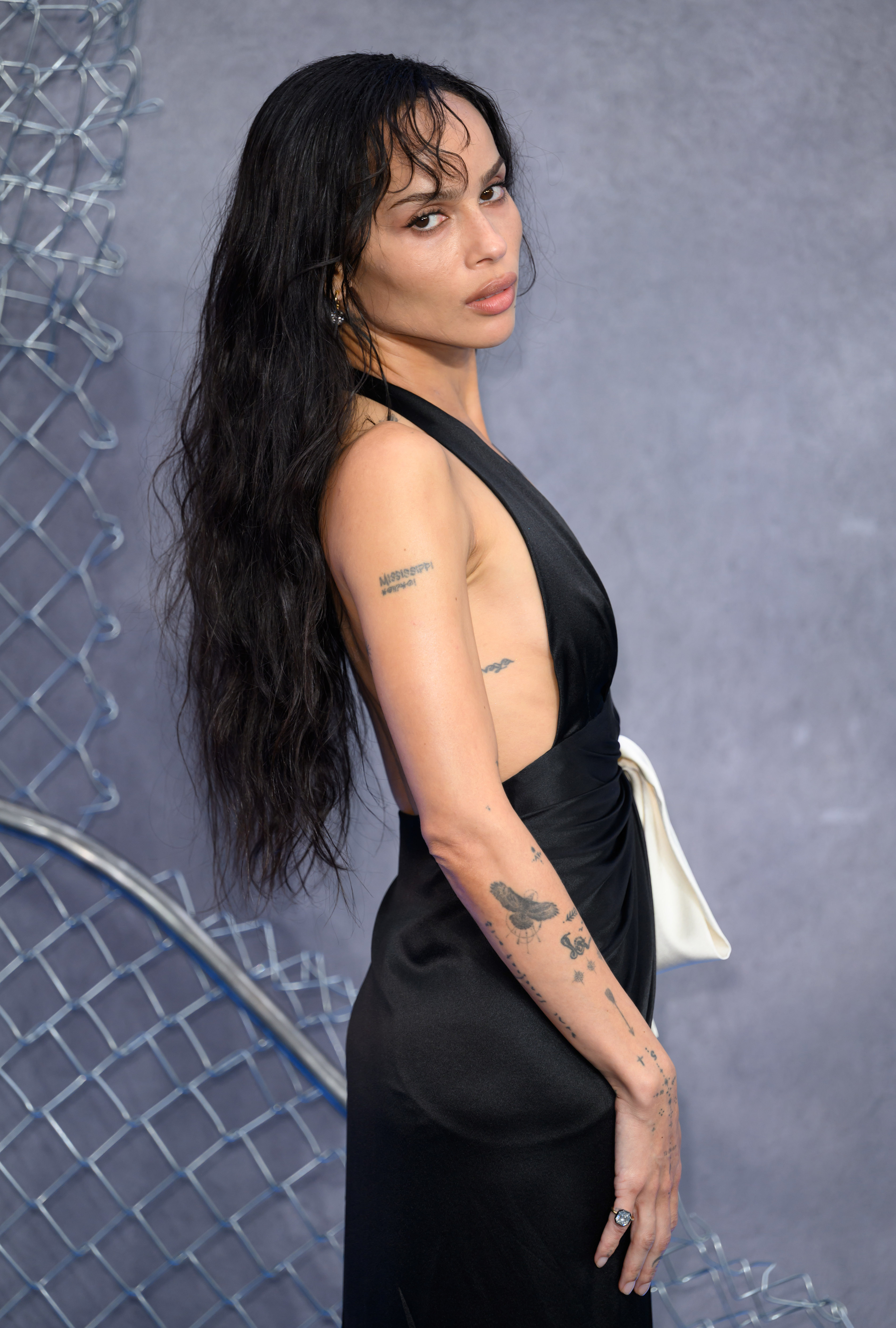 Zoë Kravitz posed for a close-up in her black halter gown, offering a side view that highlighted her tattoo collection, the gown's open back, and the sculptural bow tied at her waist. Her long, wet-styled hair and minimal makeup completed the sharp, sculpted look.