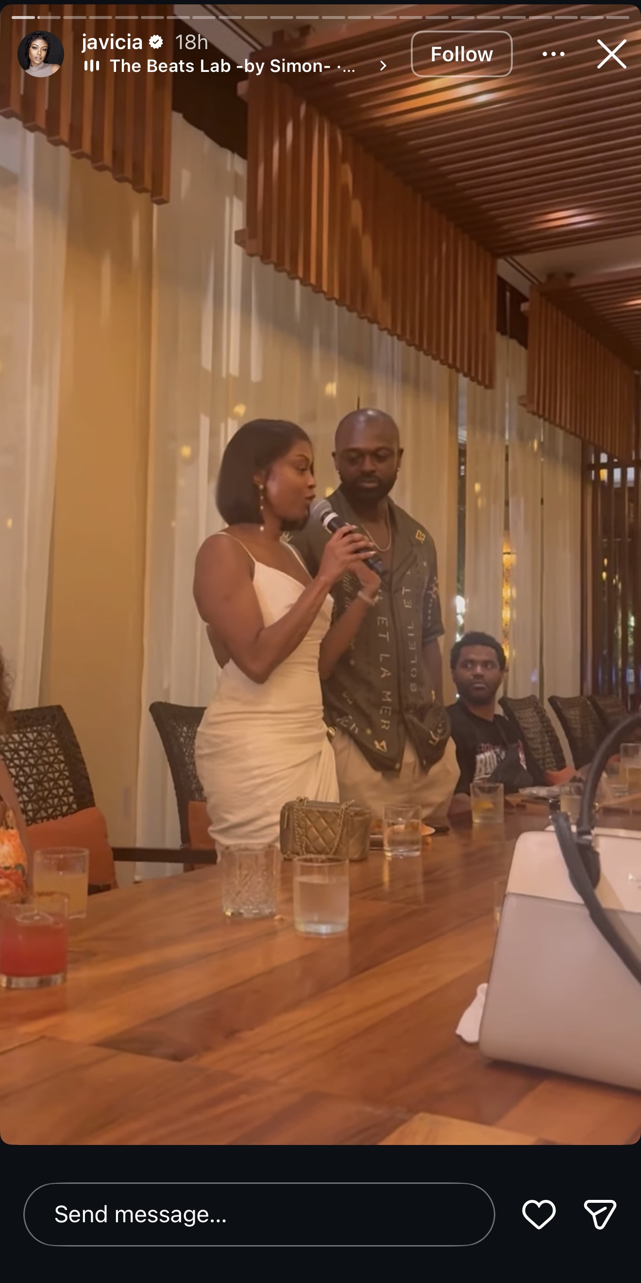 Javicia Leslie stands beside her groom, Nana-Yaw Asamoah, at a warmly lit reception table, holding a microphone as she speaks. | Source: Instagram/javicia