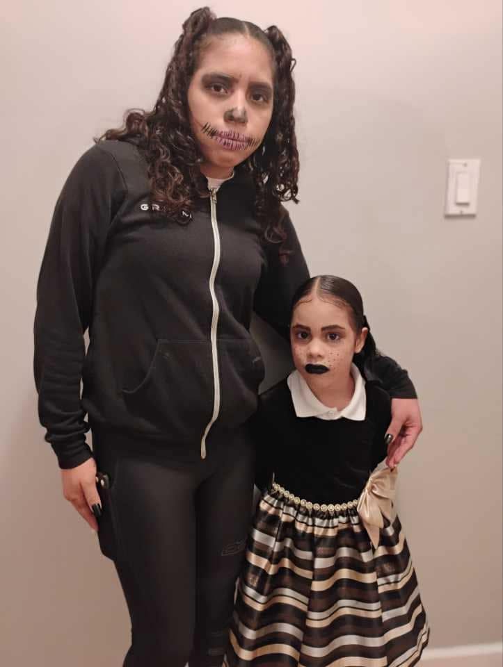 Eddimar Paola Hernández Chacón and her older sister showed off their spooky costumes while celebrating Halloween in 2025. Eddimar embraced a Wednesday Addams-inspired look with a white-collared black dress, striped satin flared skirt, sleek parted hair, and dark lipstick, standing beside her sister, who sported half-up pigtails, an all-black zip-up outfit, and dramatic skeletal face paint. | Source: Facebook/Morena Esa