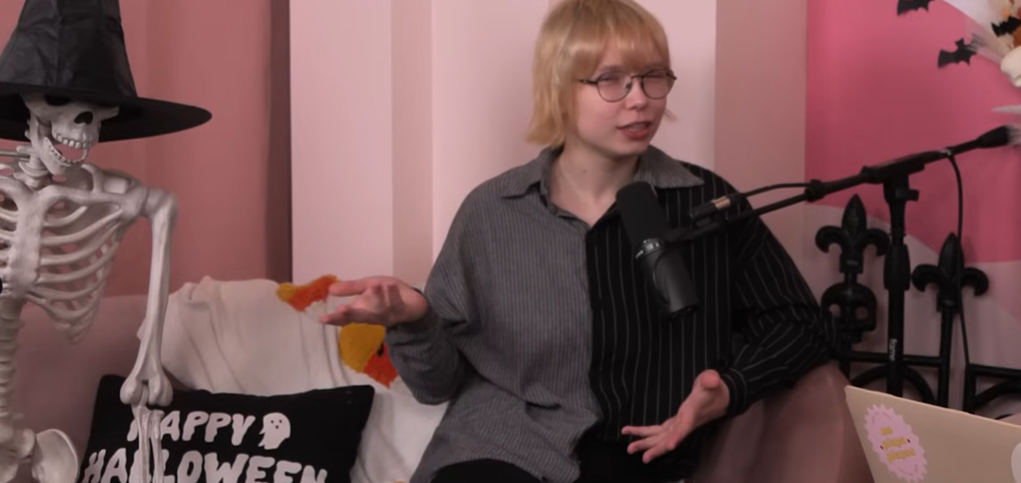With a relaxed posture, Stevie continues explaining her thoughts while seated beside a Halloween prop skeleton, posted in November 2023 | Source: YouTube/justalittleshadypodcast