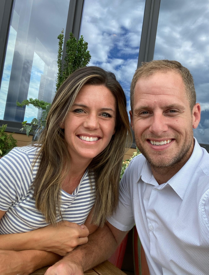 Caleb and Ashley Flynn are seated with large windows behind them reflecting a partly cloudy sky. | Source: Facebook/AshleyFlynn