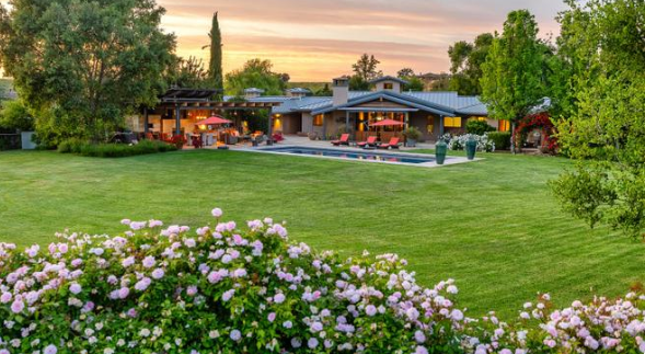 A wide view of the property shows the modern home, swimming pool, and expansive landscaped lawn framed by flowering shrubs and mature trees. | Source: Redfin