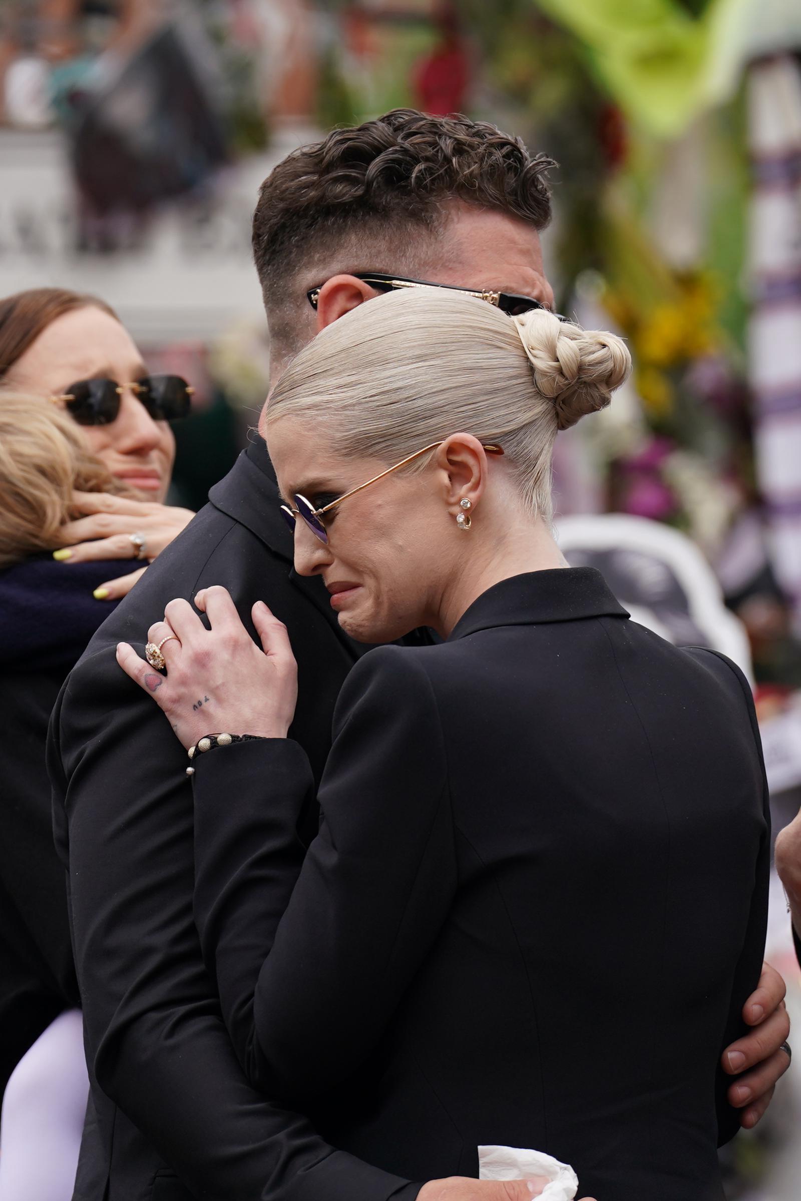 One of the final public moments involving Kelly and her father came after Ozzy's death. During the funeral procession in Birmingham, Kelly, dressed in black and wearing sunglasses, is seen hugging a man while appearing emotional. Her family stood nearby as they looked at the flowers and messages left in Ozzy's memory. | Source: Getty Images