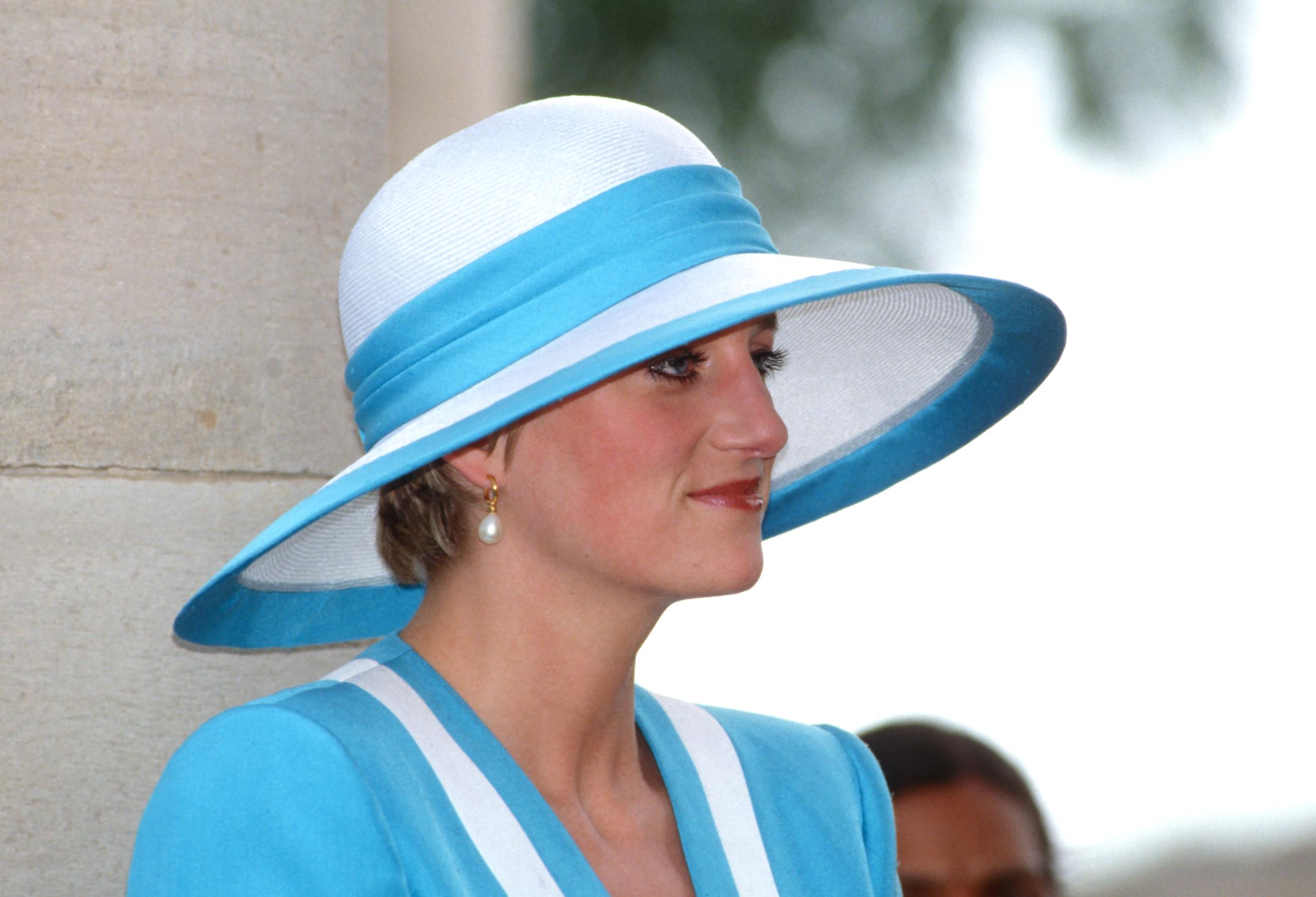 In a close-up from her 1992 visit to the Delhi War Cemetery, Princess Diana’s serene expression takes center stage. Wearing a refined blue and white Catherine Walker suit and a sculpted Philip Somerville hat, the camera captures the quiet dignity on her face, framed elegantly by her signature style.