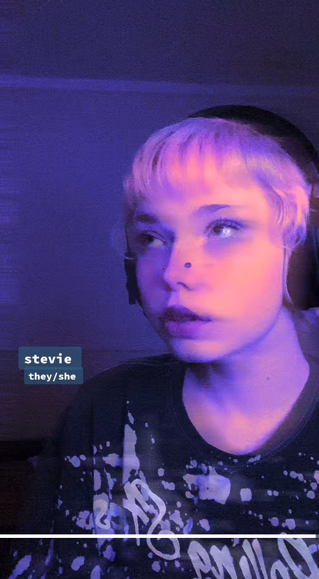Now appearing with short lavender hair, Stevie is under purple lighting wearing headphones and a splatter-print shirt. Her label now shows the name Stevie with they/she pronouns. | Source: TikTok/st0nedc0w
