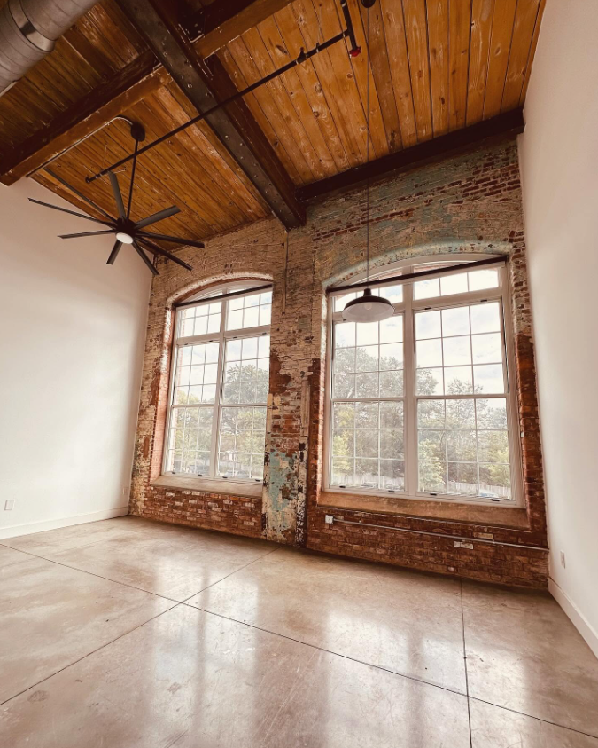 A larger loft highlights the property’s signature industrial architecture, with soaring arched windows, exposed brick walls and a wood-paneled vaulted ceiling. | Source: Facebook/Judson Mills Loft