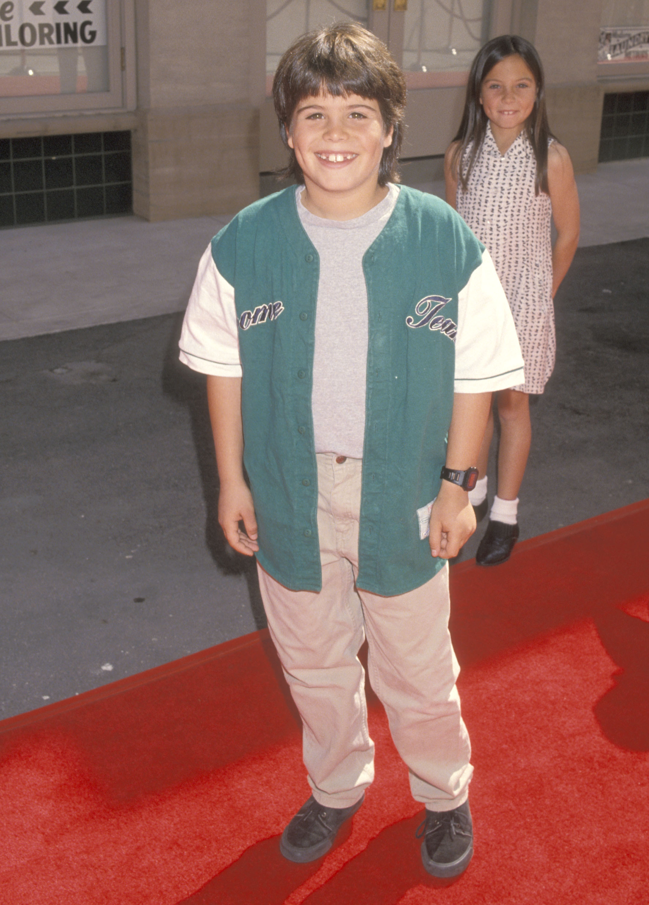 The young actor smiles on the red carpet in a green baseball-style jersey and beige pants, showing off his casual childhood style during his early Hollywood years. | Source: Getty Images.