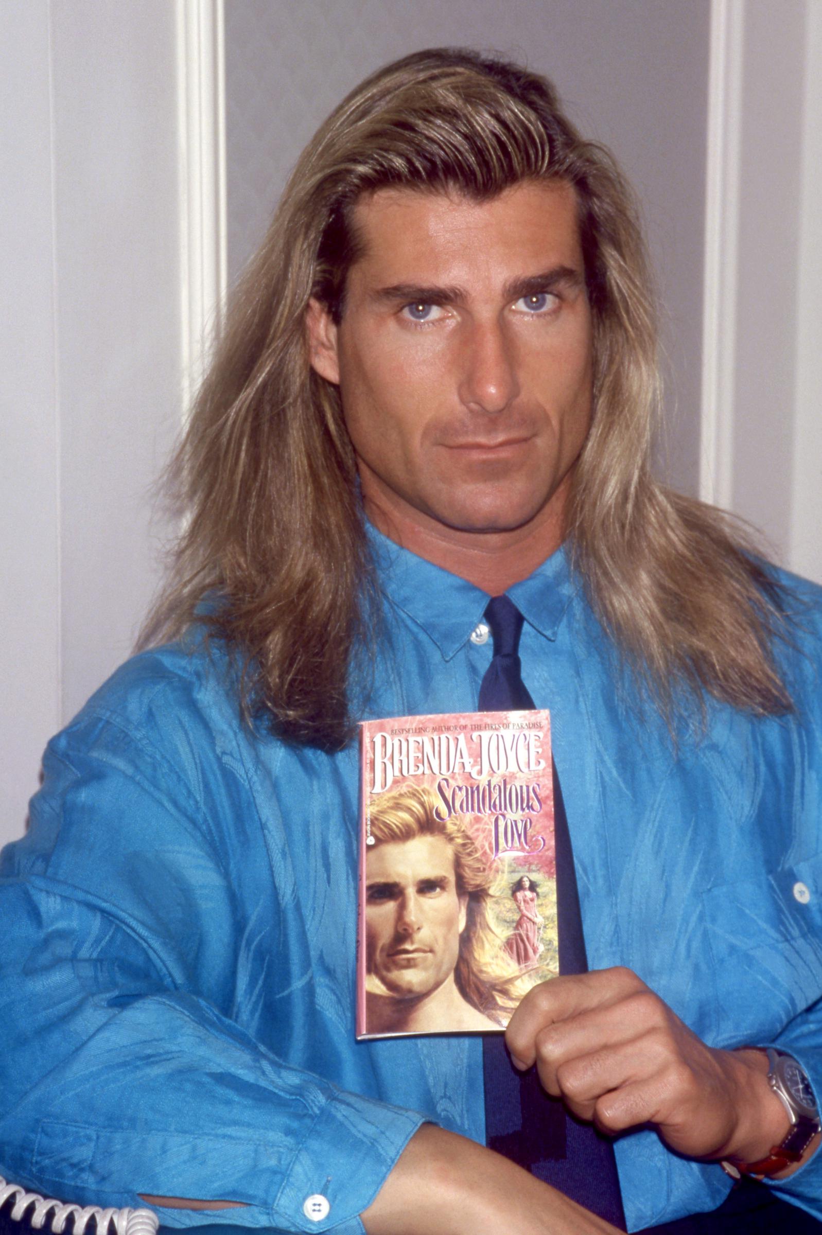 But he would soon find his fame in the most unexpected place. In this photo, the iconic romance book cover star posed for a portrait with Brenda Joyce's book "Scandalous Love" in New York, New York, on November 8, 1992. | Source: Getty Images