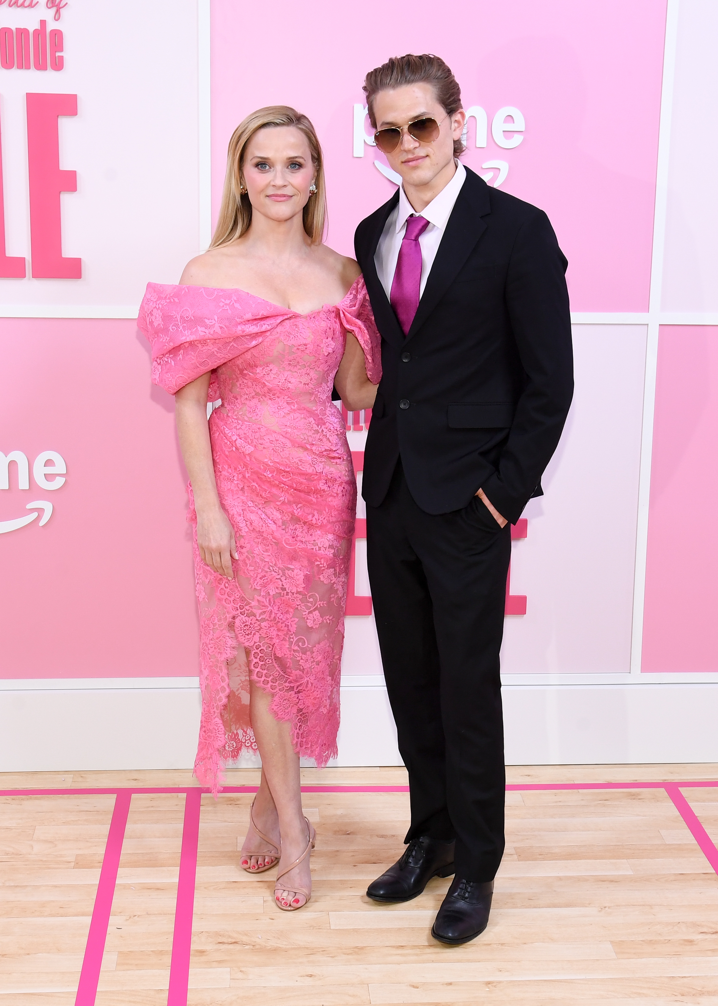 Reese Witherspoon and Deacon Phillippe pose at Prime Video's "Elle" New York premiere, coordinated against the pink backdrop as he wears a black suit and magenta tie. | Source: Getty Images