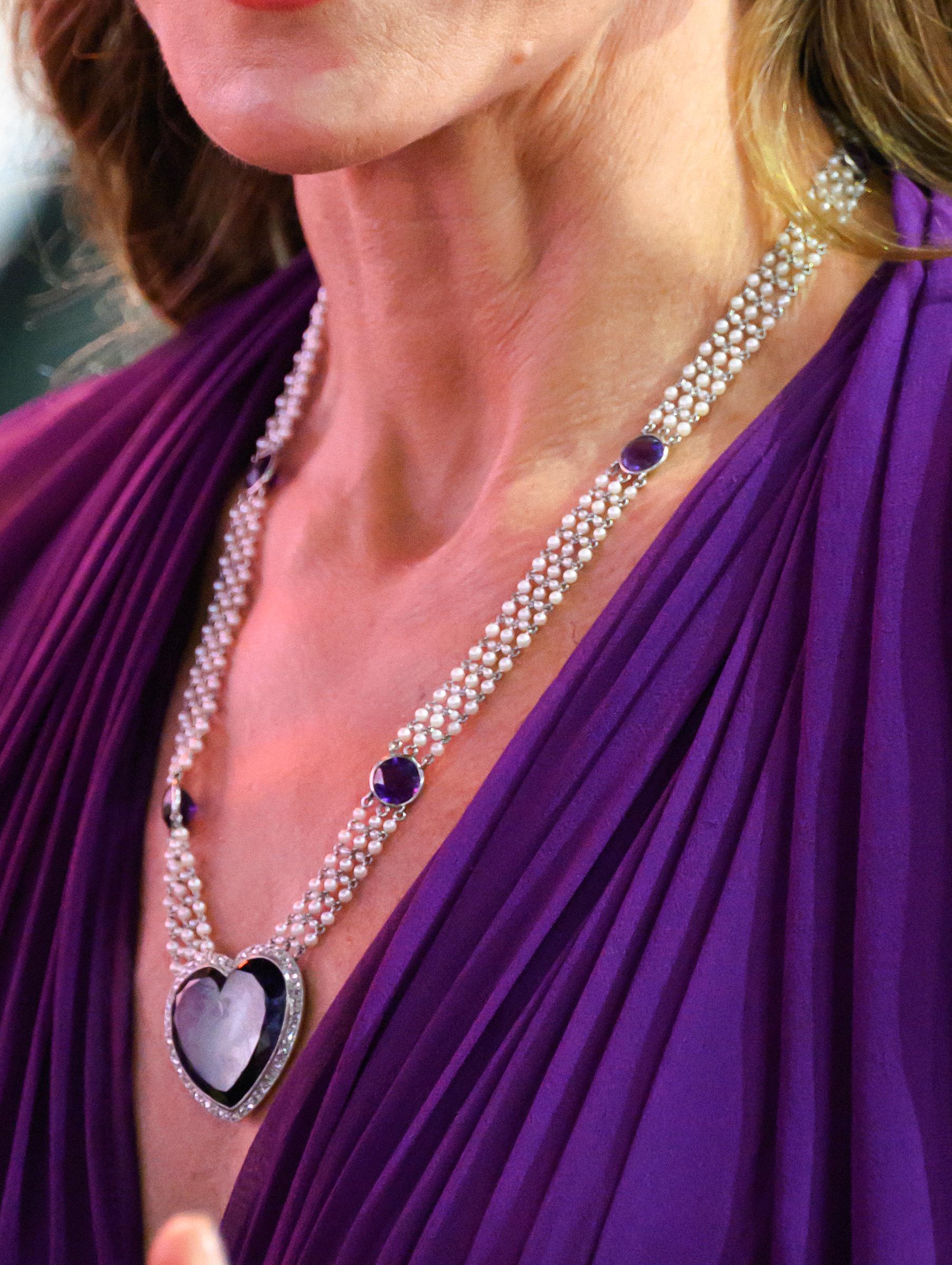 A close-up shows Catherine's necklace against the plunging neckline of her purple gown. The multi-strand design features purple stones and a large heart-shaped pendant.