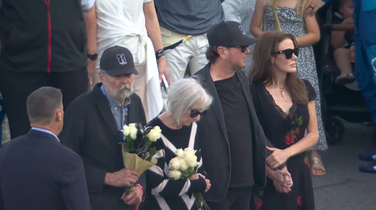 Kyle Busch’s parents, Tom and Gaye, stand with Kurt Busch and his girlfriend, Lyda Moore, during the tribute ceremony on May 24, 2026 | Source: YouTube/NASCAR