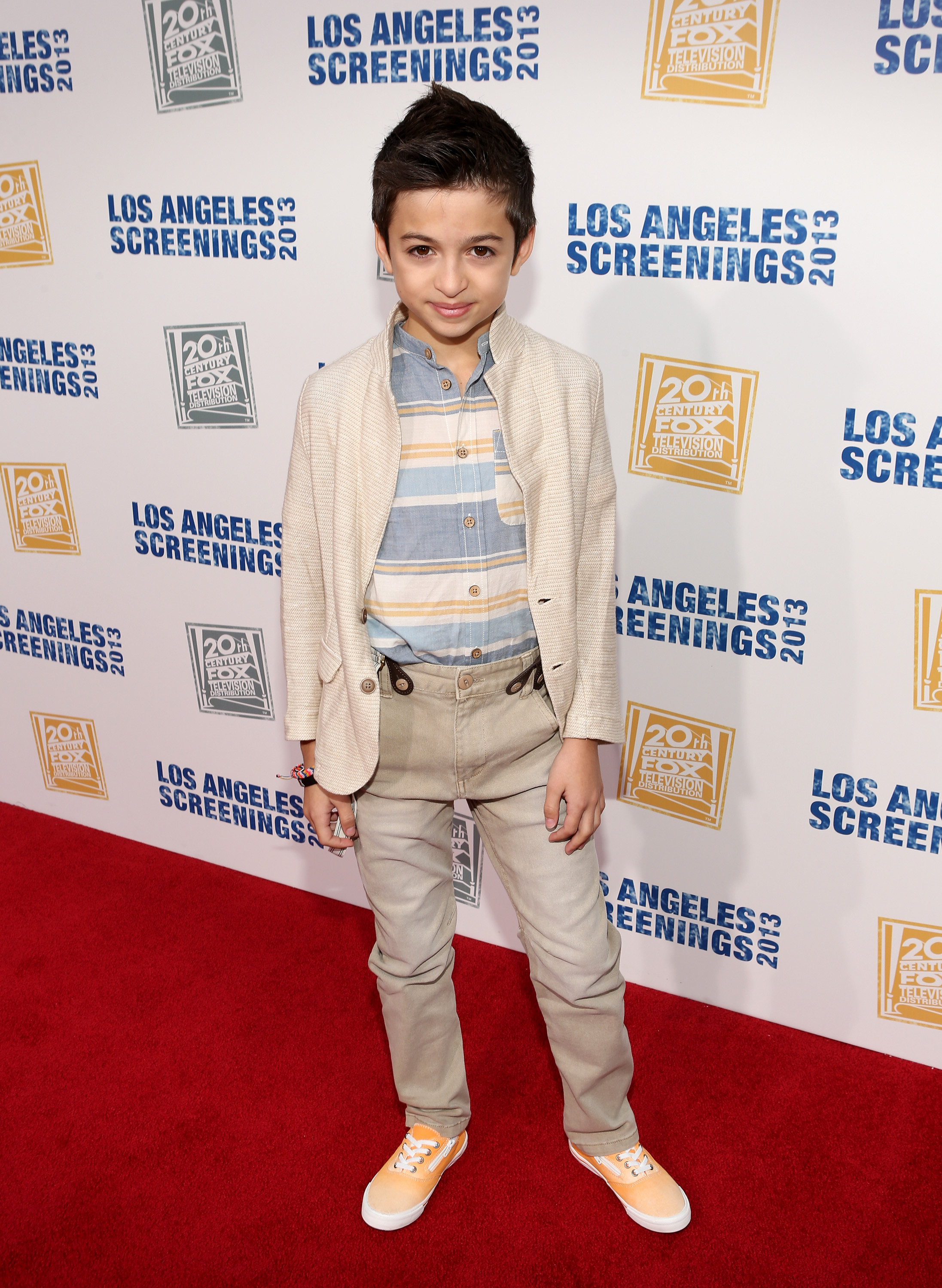 She poses on the red carpet at Twentieth Century Fox Television Distribution's 2013 LA Screenings Lot Party in Los Angeles, California, wearing a cream blazer, a striped shirt, beige pants, and orange sneakers. | Source: Getty Images