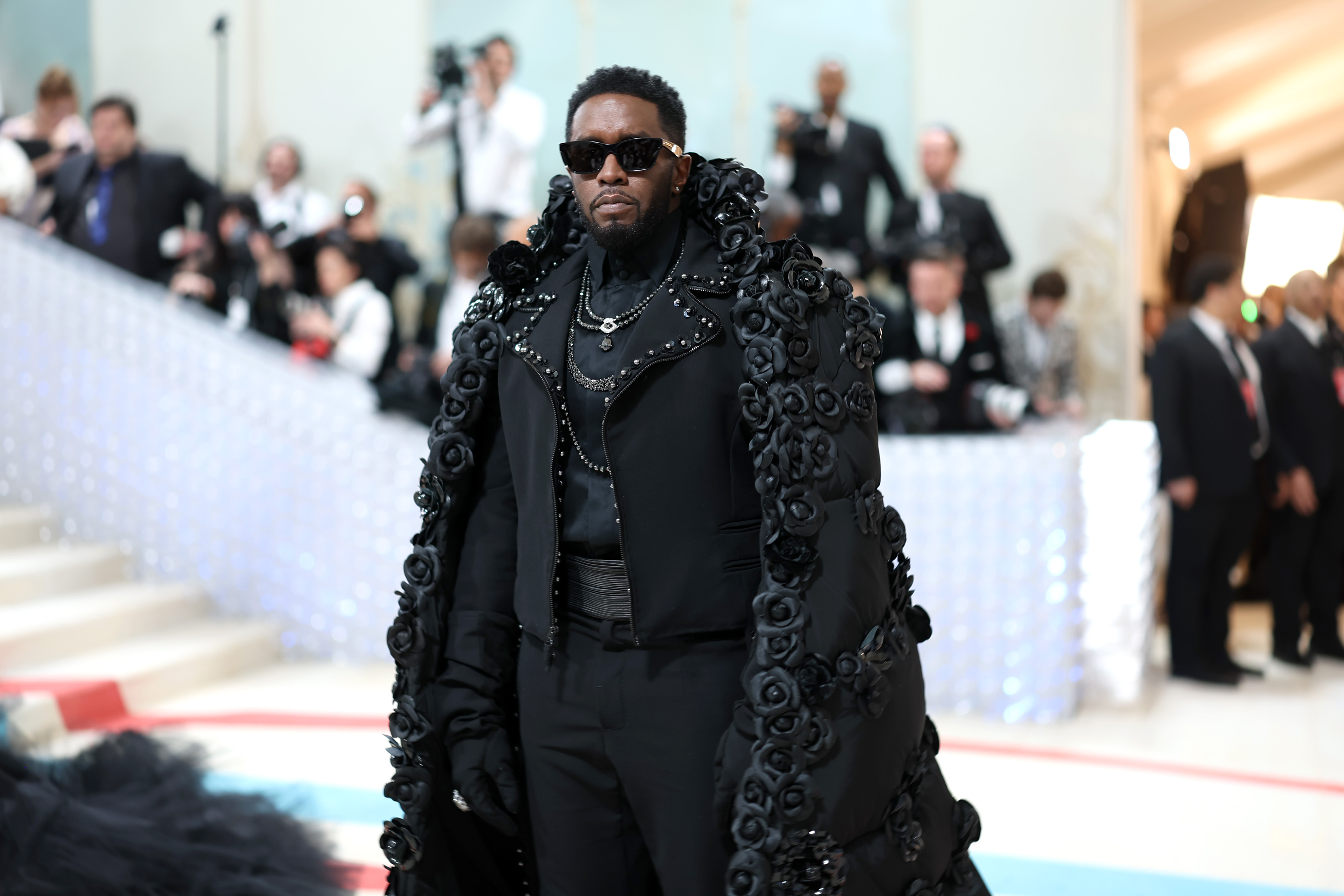 Sean "Diddy" Combs makes a powerful entrance at the Met Gala on May 1, 2023, in New York City, wearing an all-black ensemble with an oversized cape covered in textured floral embellishments.