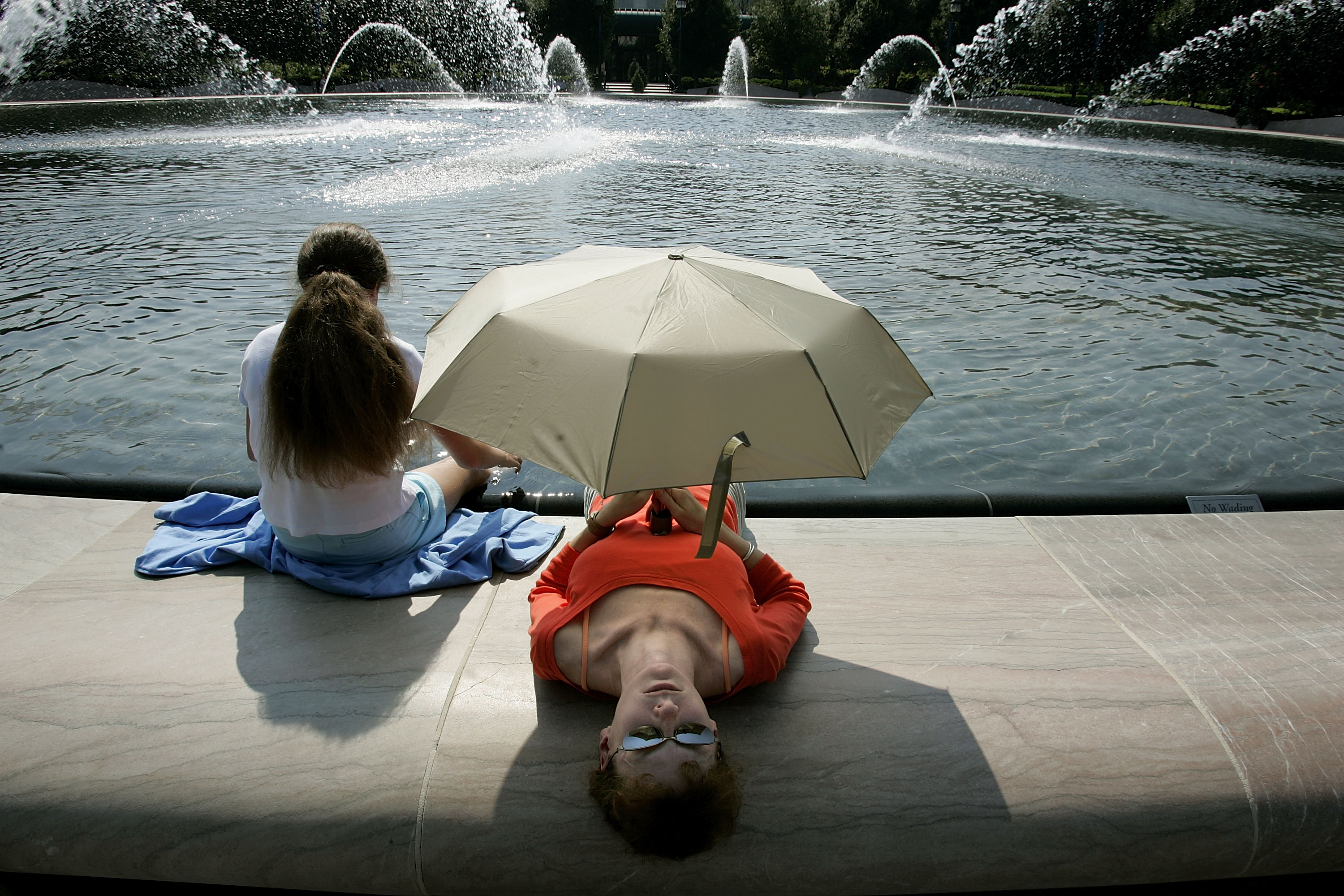 A mother and daughter take shade under an umbrella by a fountain during extreme heat in Washington, D.C., on July 26, 2005 | Source: Getty Images