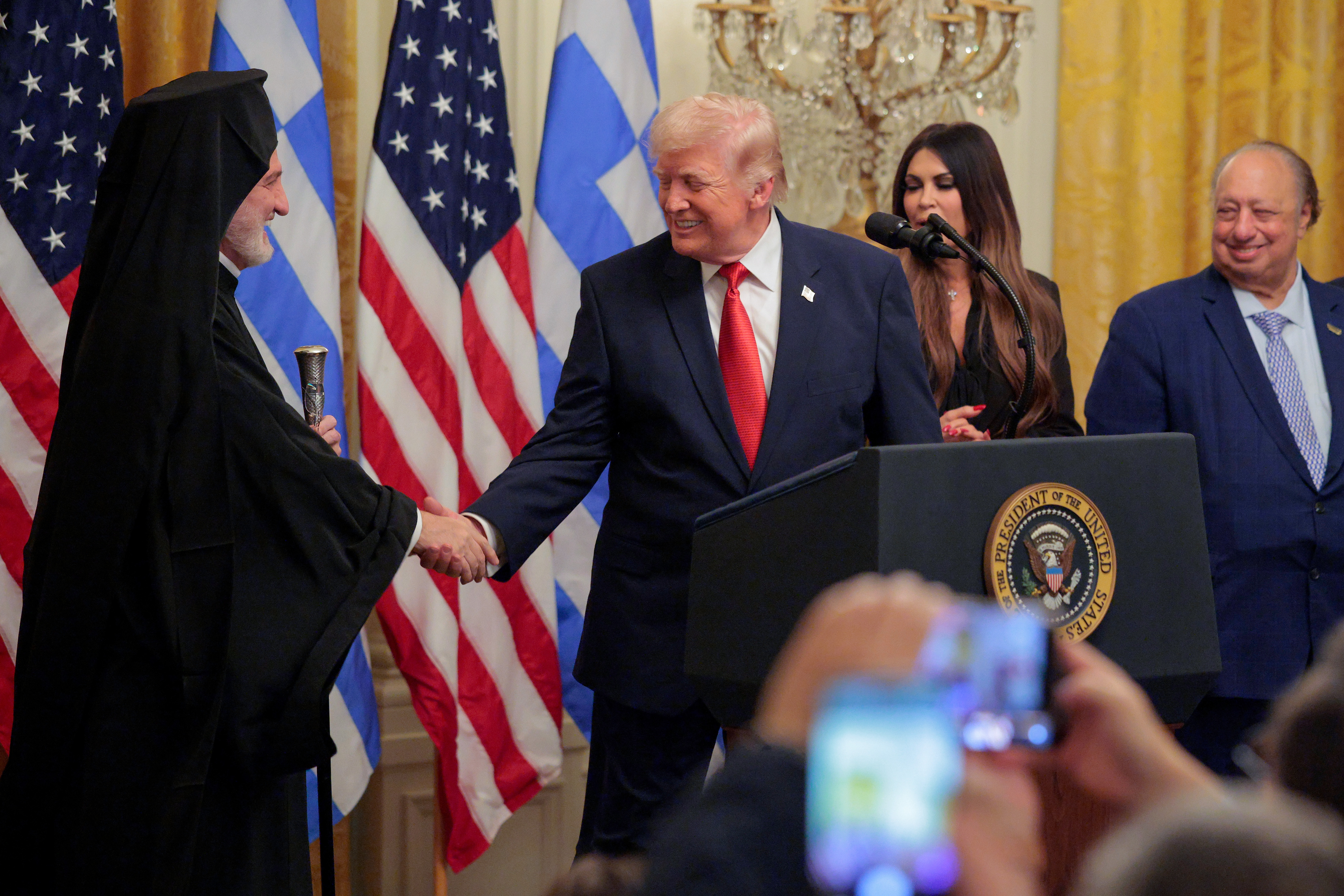President Donald Trump greets Archbishop Elpidophoros during the Greek Independence Day celebration as Kimberly Guilfoyle, John Catsimatidis and Margo Catsimatidis look on from the stage. | Source: Getty Images