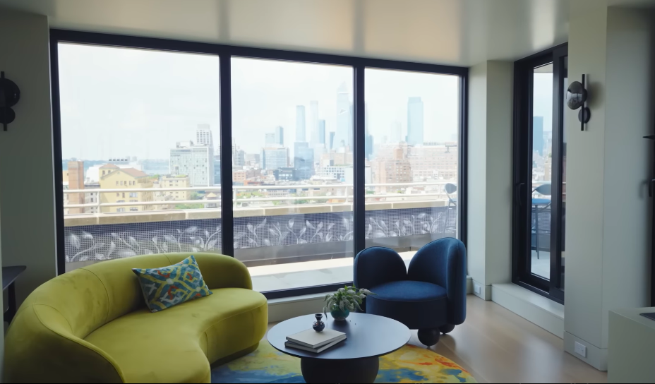 The enlarged windows make Manhattan feel less like scenery and more like another wall of the living room. A lime-green sofa and navy chair keep the spectacular outlook from stealing every bit of attention. | Source: YouTube/Architectural Digest