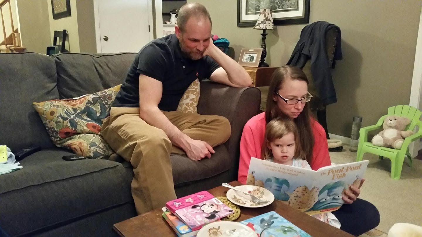 Nicole Heiser shares a quiet family moment, reading the children's book "The Pout-Pout Fish" to a little girl while a man watches from the couch. | Source: Nicole Heiser / Facebook.