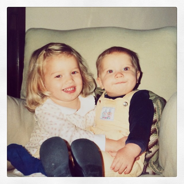 Rosie Alice Huntington-Whiteley cuddles up with a baby sibling in a sweet childhood snapshot, both smiling for the camera. | Source: Instagram/rosiehw