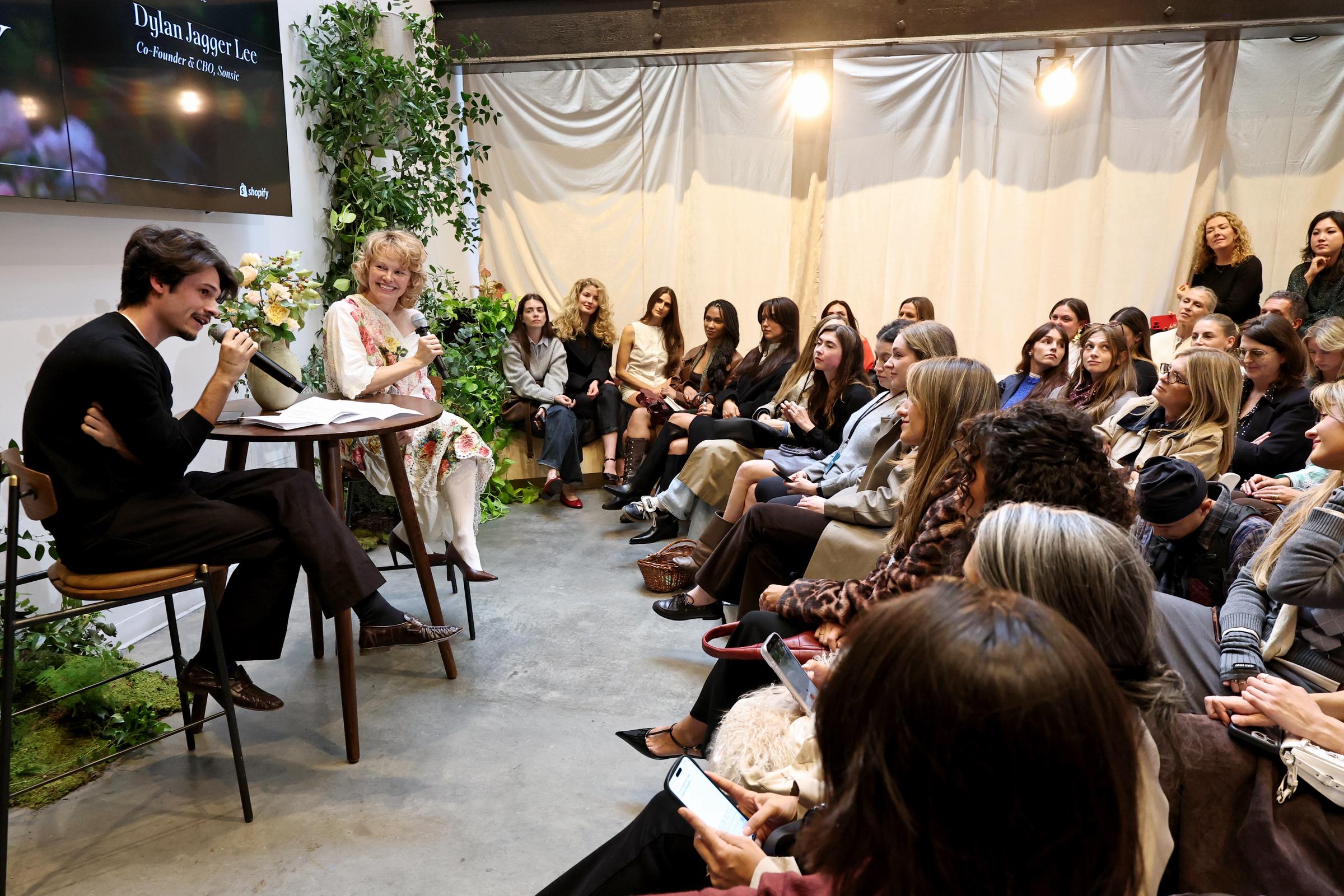 Dylan and Pamela appear in conversation during the "Sonsie Garden" panel in New York on October 24, 2025. Both are seated with microphones in hand, framed by greenery and a vase of roses on the table between them.
