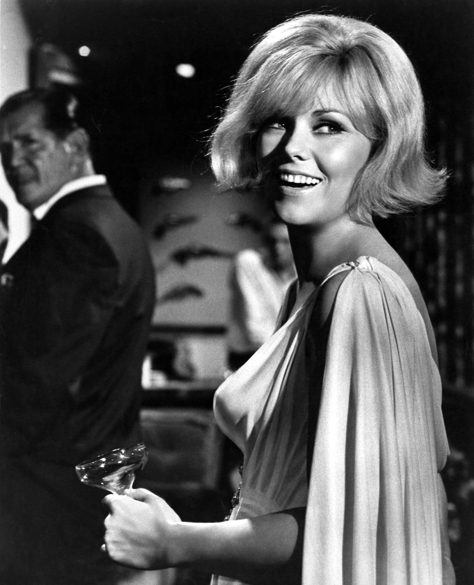 Kim Novak smiles while holding a cocktail glass on the set of The Legend of Lylah Clare, wearing a flowing evening dress. | Source: Getty Images