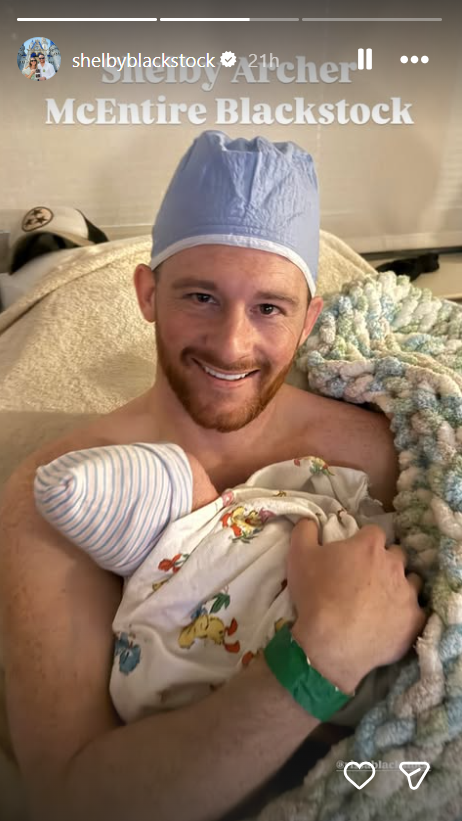 Shelby Blackstock beams from a hospital bed while sharing skin-to-skin bonding time with his newborn son, Shelby Archer McEntire Blackstock, in an Instagram Story shared on October 21, 2026. The new father wears a blue surgical scrub cap while cradling his baby boy, who is swaddled in a patterned nursery blanket and a striped newborn beanie. | Source: Instagram/shelbyblackstock