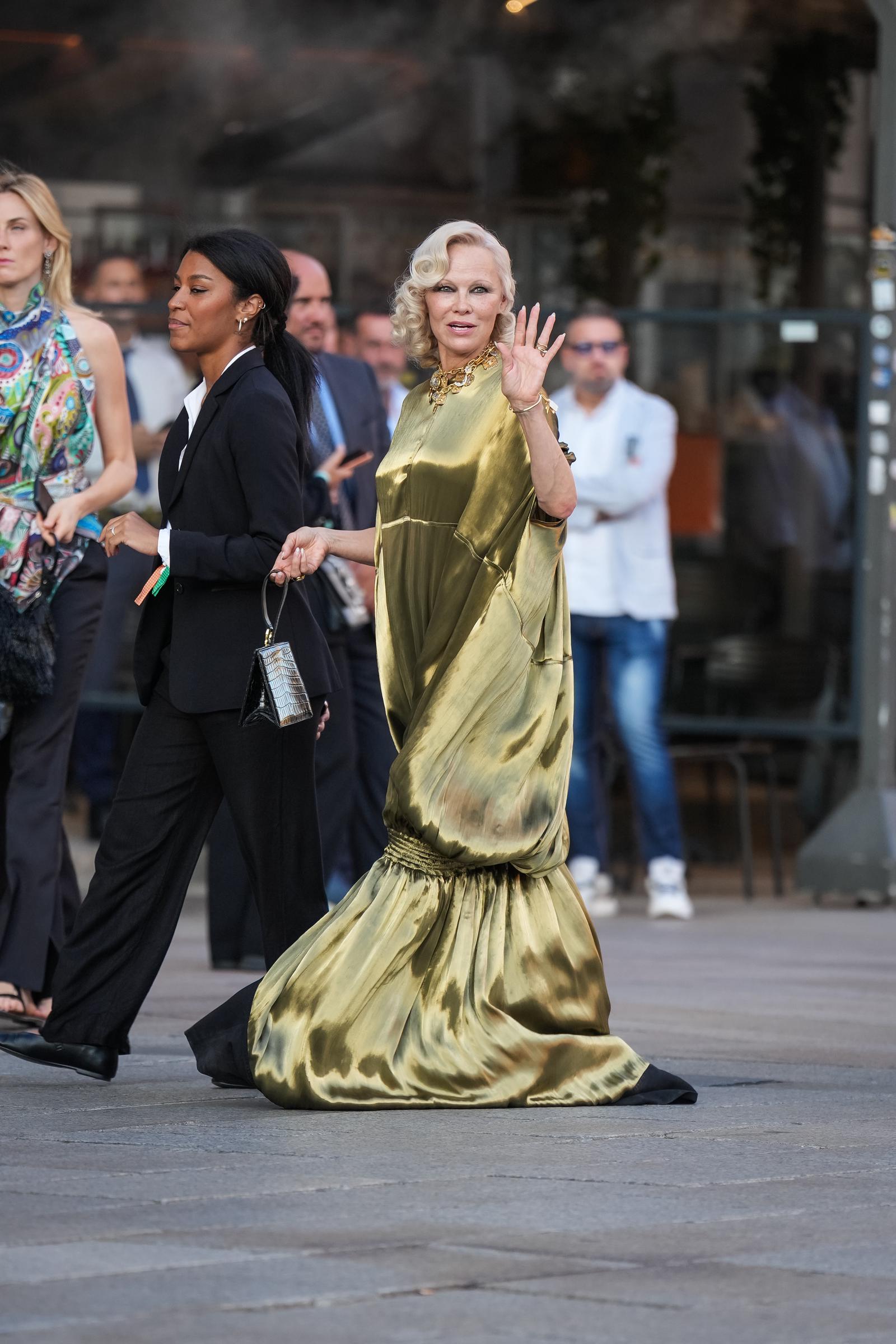 Anderson smiles and waves while arriving in Milan, as the flowing fabric of her metallic gown trails behind her. Her appearance came during Milan Fashion Week's Spring/Summer 2027 womenswear season. | Source: Getty Images