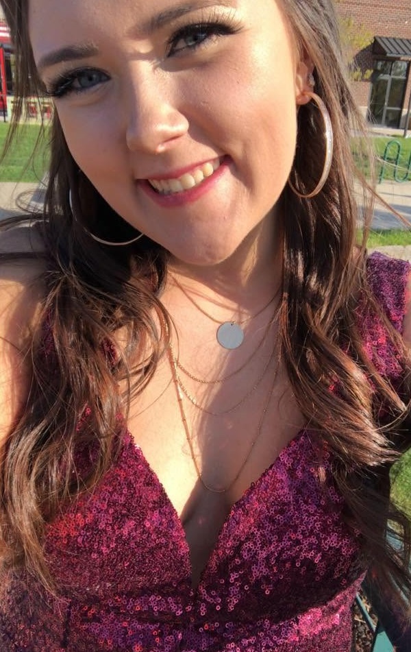 Hannah Jorgensen smiles outdoors in a close-up selfie while wearing a sparkling maroon sequined dress, layered delicate necklaces, and hoop earrings. | Source: Facebook/Hannah Jorgensen