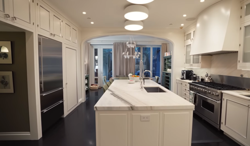This angle shows how the kitchen connects to the rest of the home. The black floors add a sharp contrast to the otherwise creamy palette. | Source: YouTube/Architectural Digest