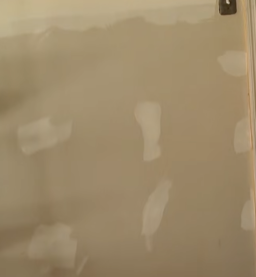 A beige wall inside the Gosselin home features several irregular white patches, possibly from repairs or removed fixtures, in footage from Kate Plus 8: Construction Prep. The image offers a glimpse of the work involved as the family prepared for changes to the children's bedrooms.