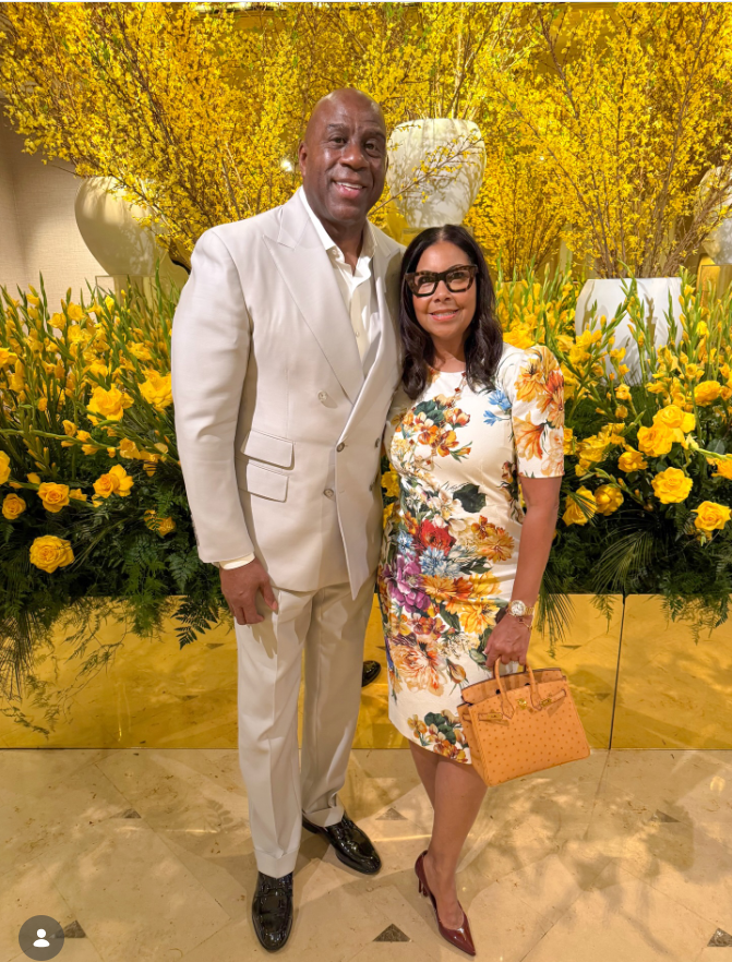 Magic Johnson and Cookie Johnson posing together at a glamorous event surrounded by vibrant yellow floral arrangements. | Source: Instagram/magicjohnson