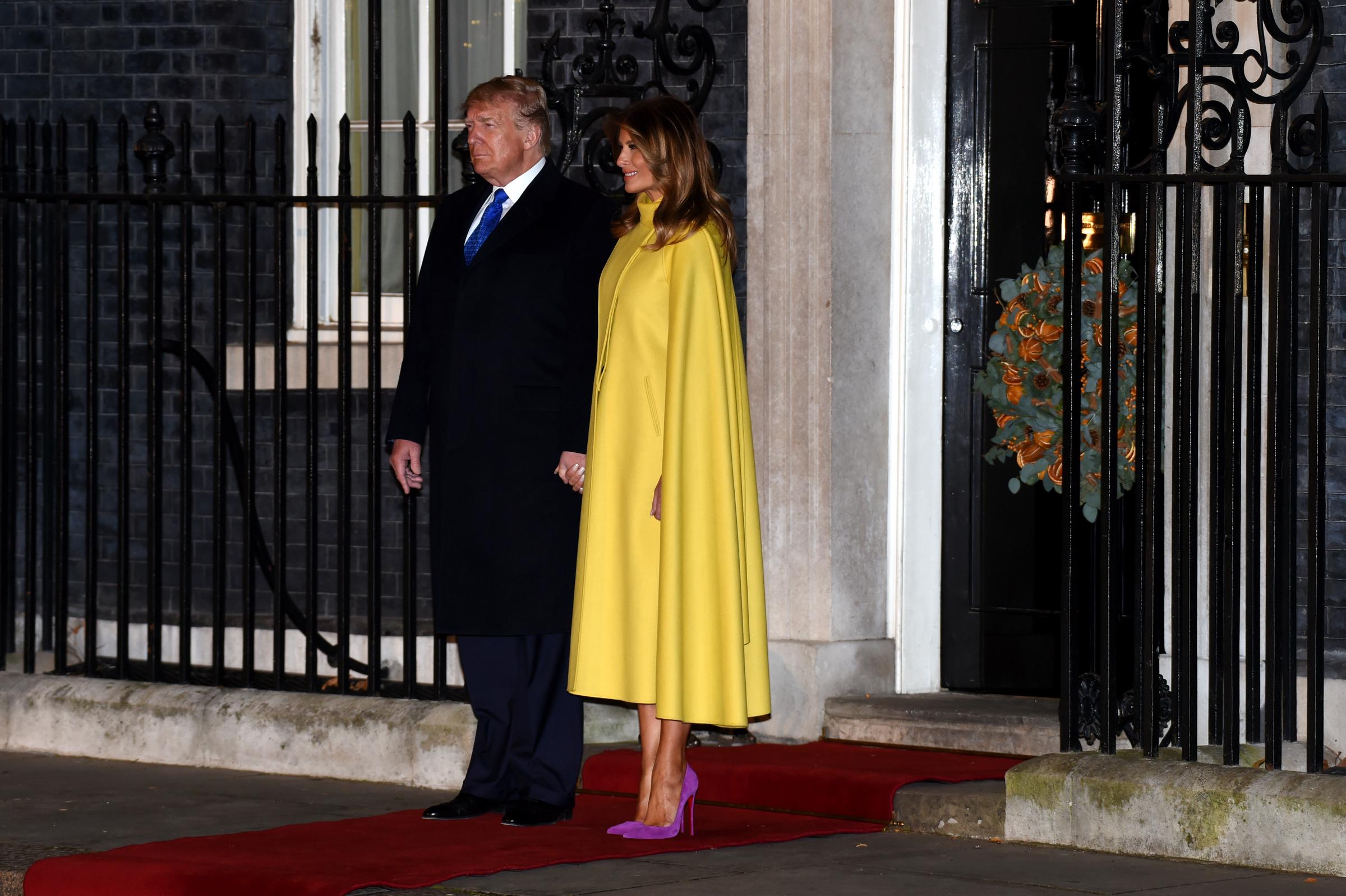 First Lady Melania Trump attends the NATO Summit reception at 10 Downing Street in London in December 2019, delivering a dramatic color-blocked look in a vibrant yellow Valentino cape coat paired with magenta suede Christian Louboutin pointed-toe stiletto pumps.