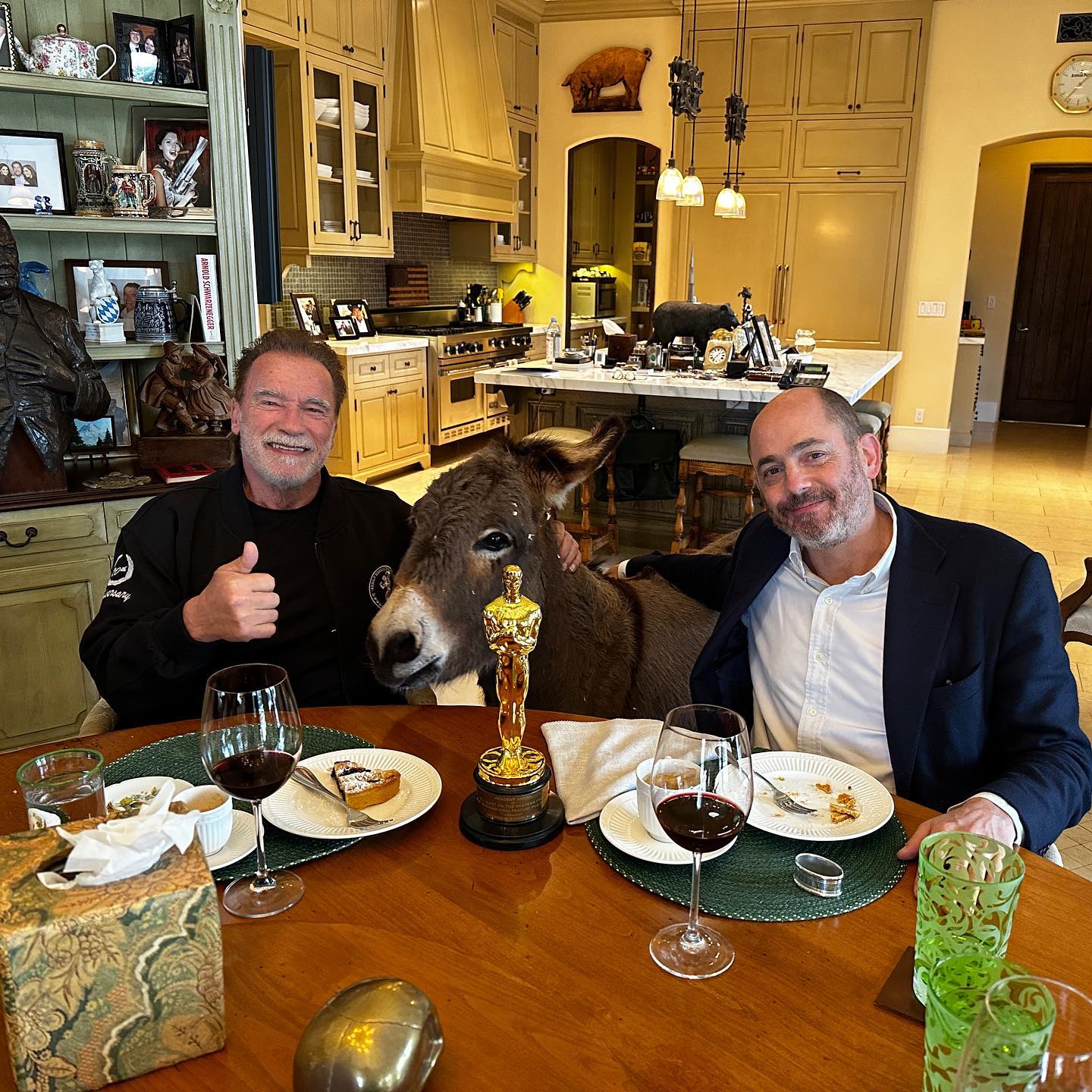 Arnold Schwarzenegger poses with a donkey, a guest, and an Oscar at the dinner table in a photo posted on April 29, 2023 | Source: Facebook/arnold