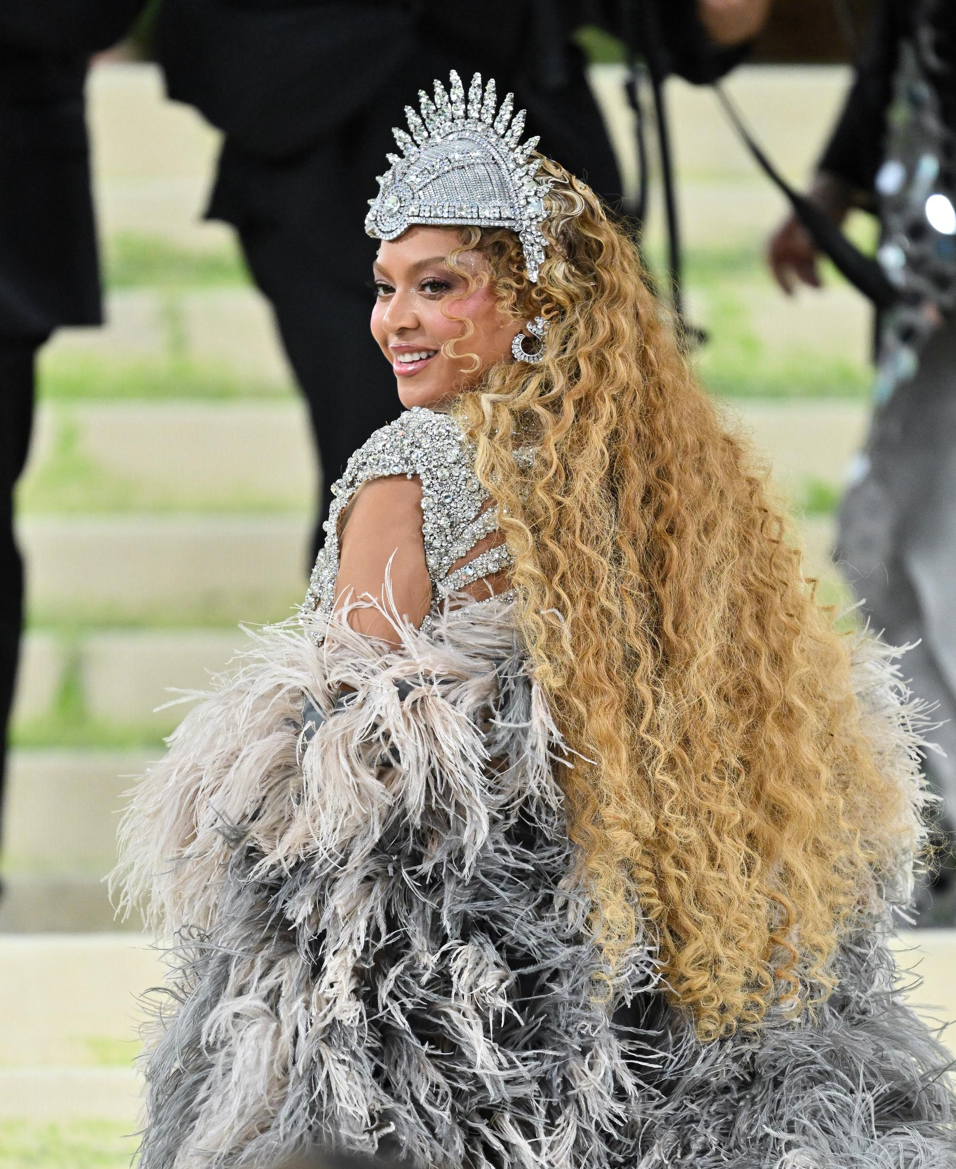 Beyoncé looks back while showing off her long curls and feathered coat at the 2026 Met Gala | Source: Getty Images