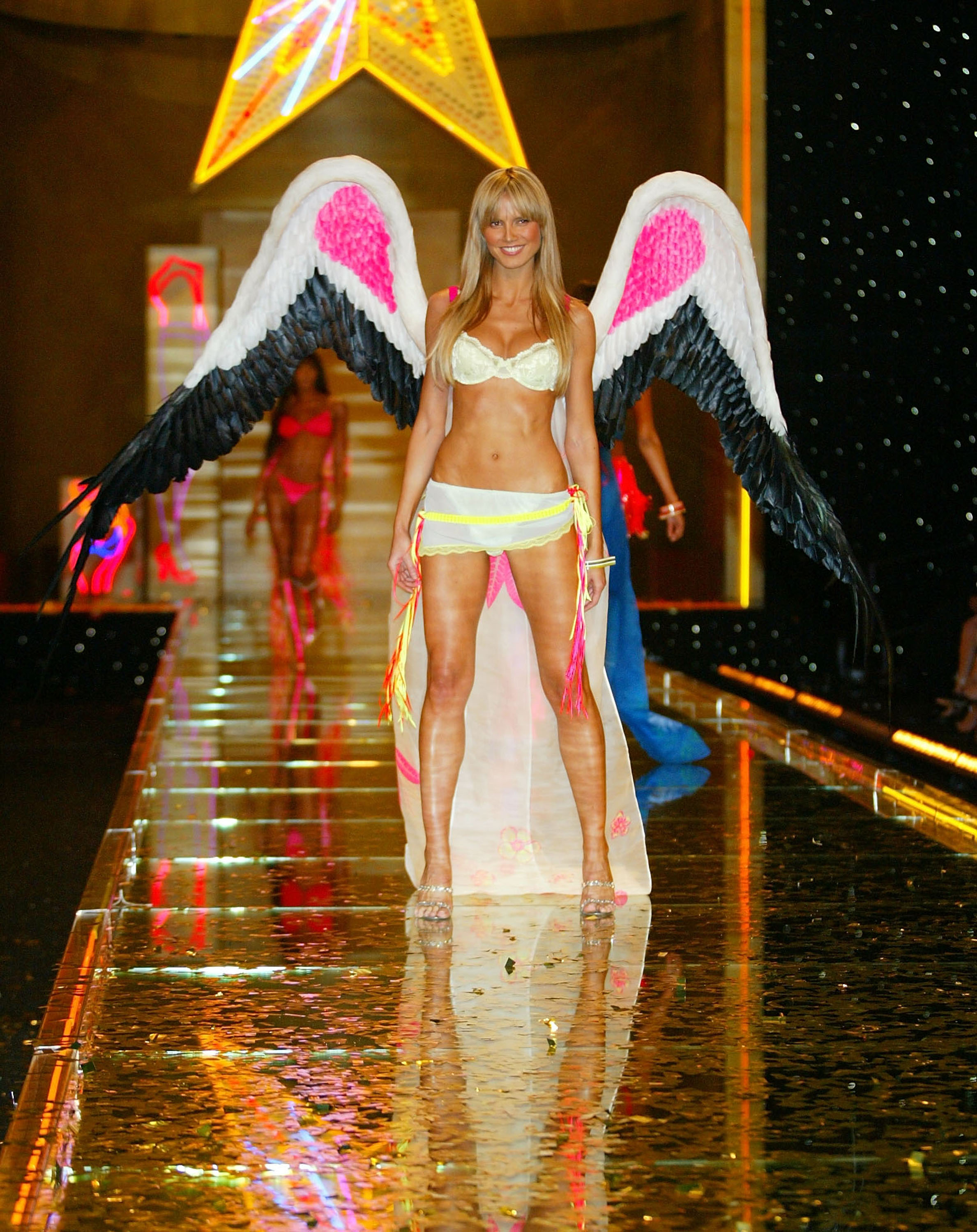 Heidi Klum wears a yellow lace bra with a sheer floral sarong and pink and black-accented wings at the Victoria's Secret Fashion Show on November 14, 2002, at the Lexington Avenue Armory in New York City.