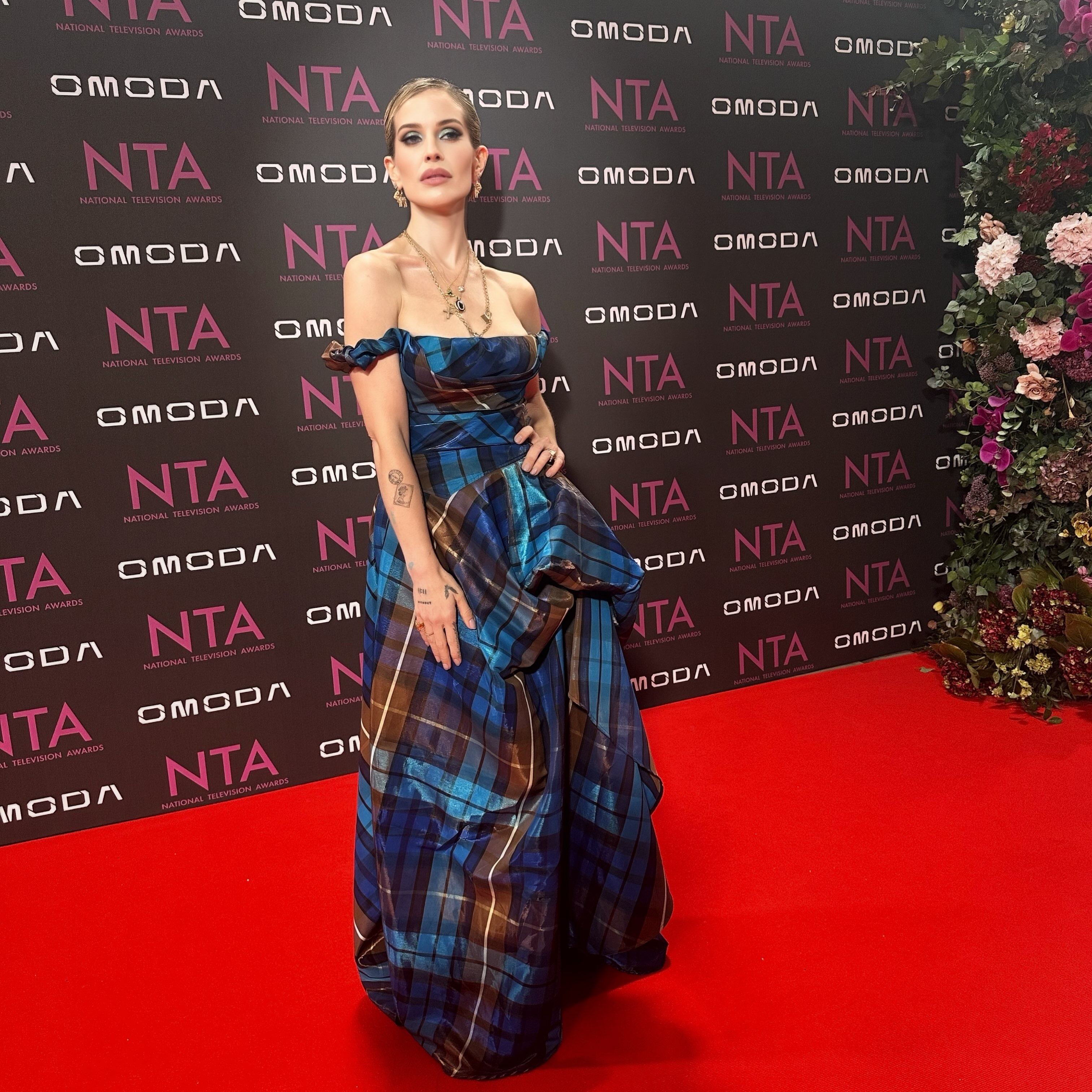Kelly showcases the asymmetric silhouette and full skirt of her €3,485 Vivienne Westwood tartan gown against the official NTA backdrop. | Source: Instagram/kellyosbourne