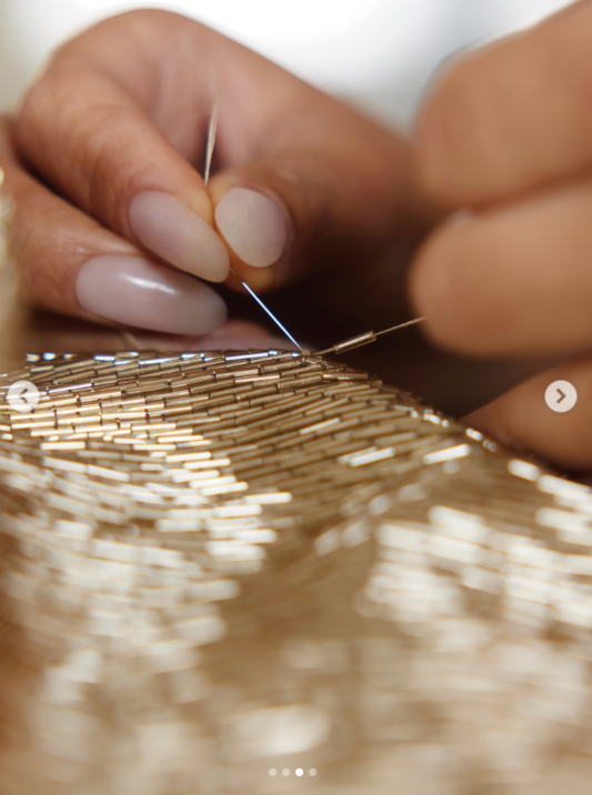 A close-up shared by Oscar de la Renta shows a craftsperson carefully hand-sewing gold bugle beads for Usha Vance's custom gown ahead of the White House China State Dinner. | Source: Instagram/oscardelarenta